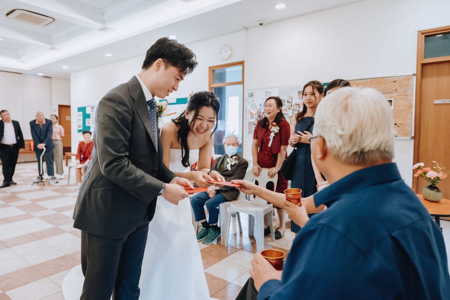 A bride and groom receive a traditional red envelope gift from an elderly guest at their wedding reception.