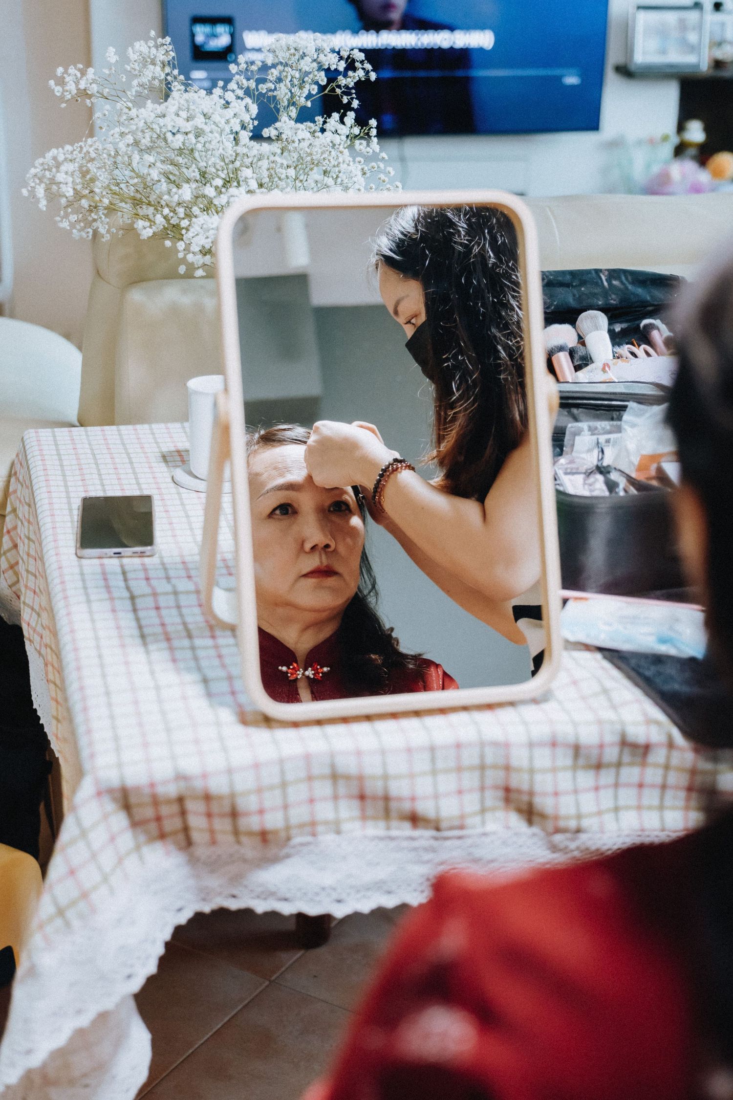A makeup artist applies makeup to a woman seated before a mirror at a wedding preparation table.
