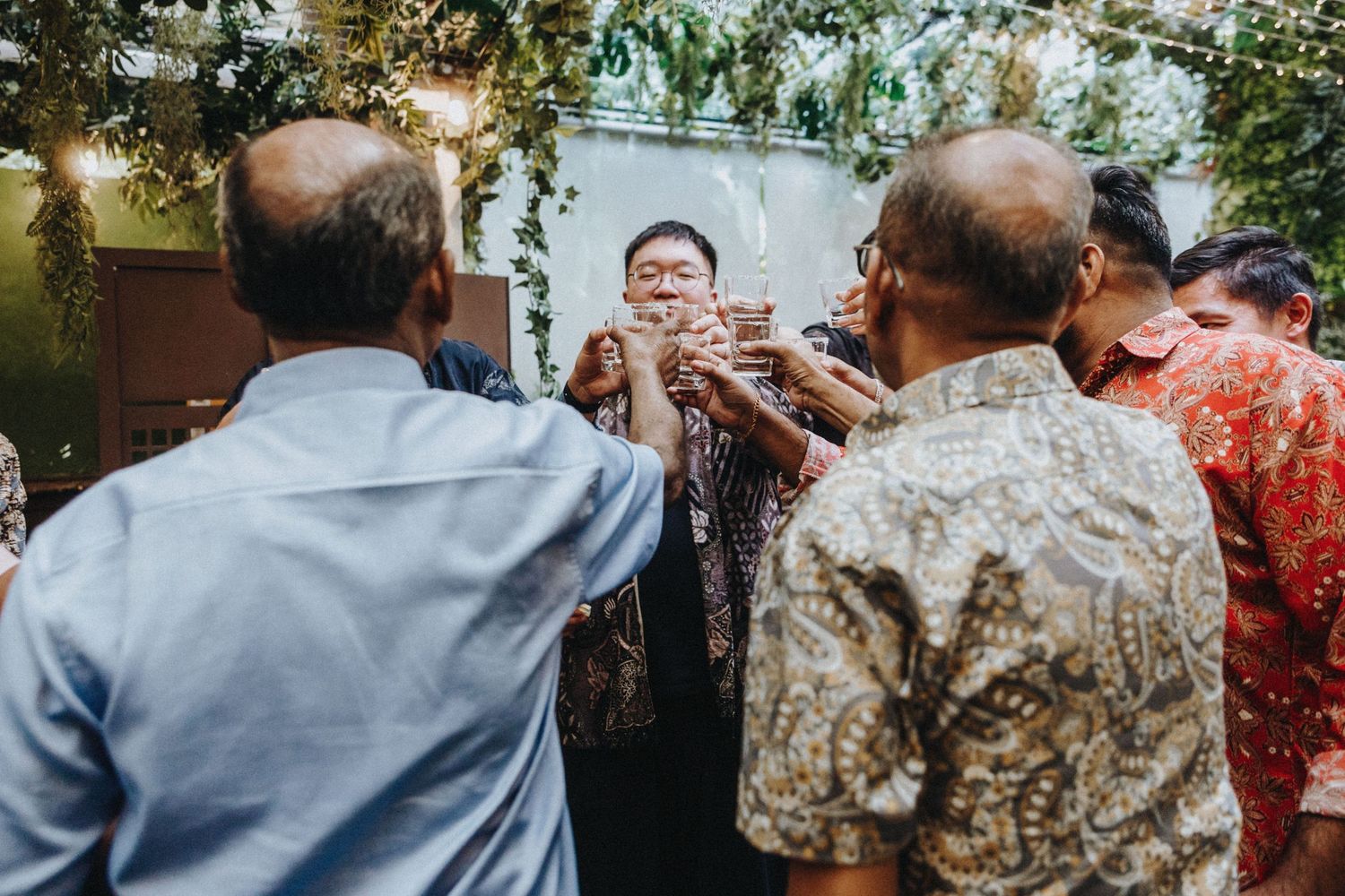 Group of wedding guests clinking glasses in a celebratory toast at a decorated reception venue.