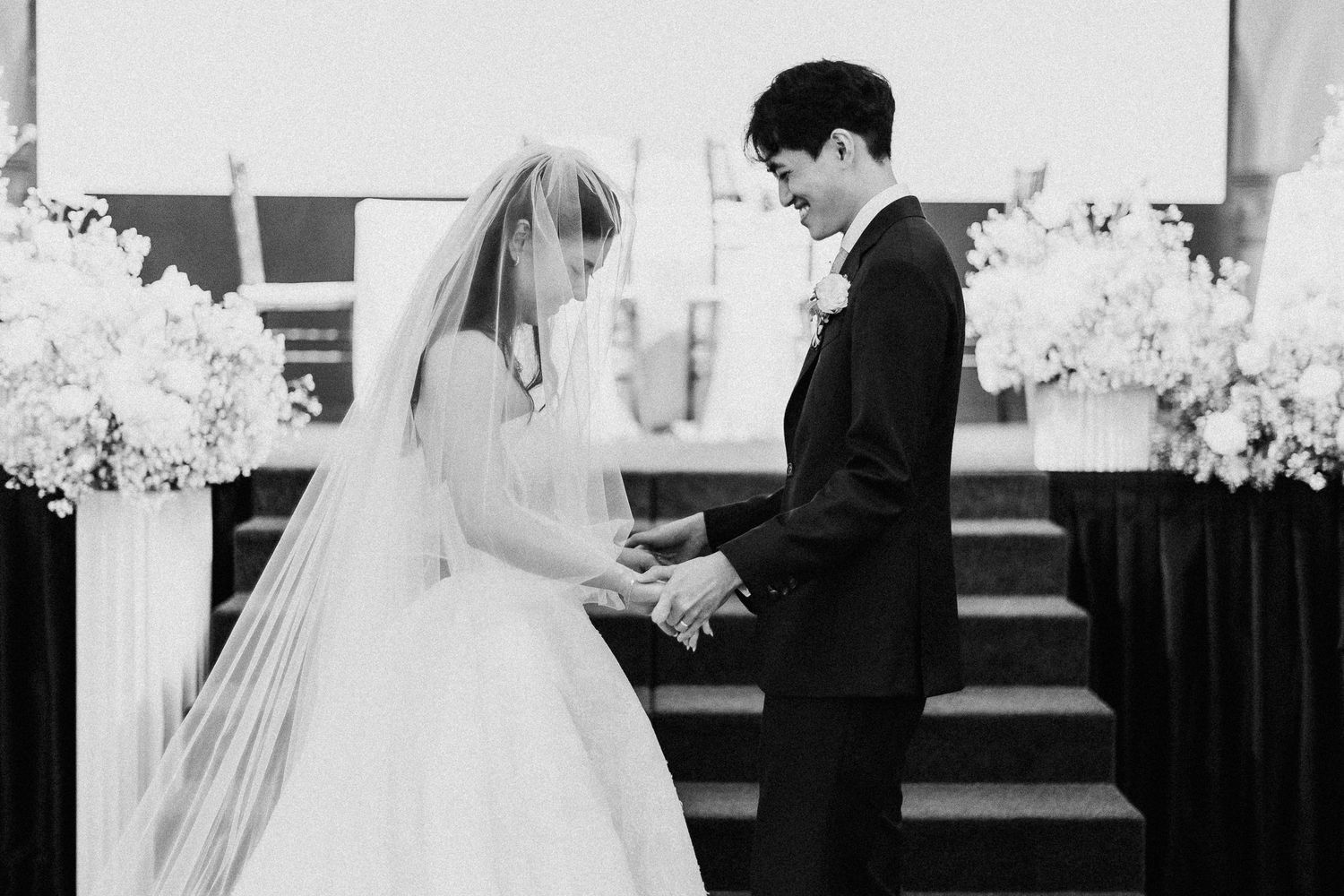 Black and white photo of a bride and groom holding hands at the altar during their elegant wedding ceremony.