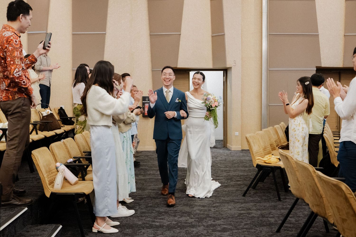 Newlyweds walking down the aisle as guests applaud in a modern wedding venue.