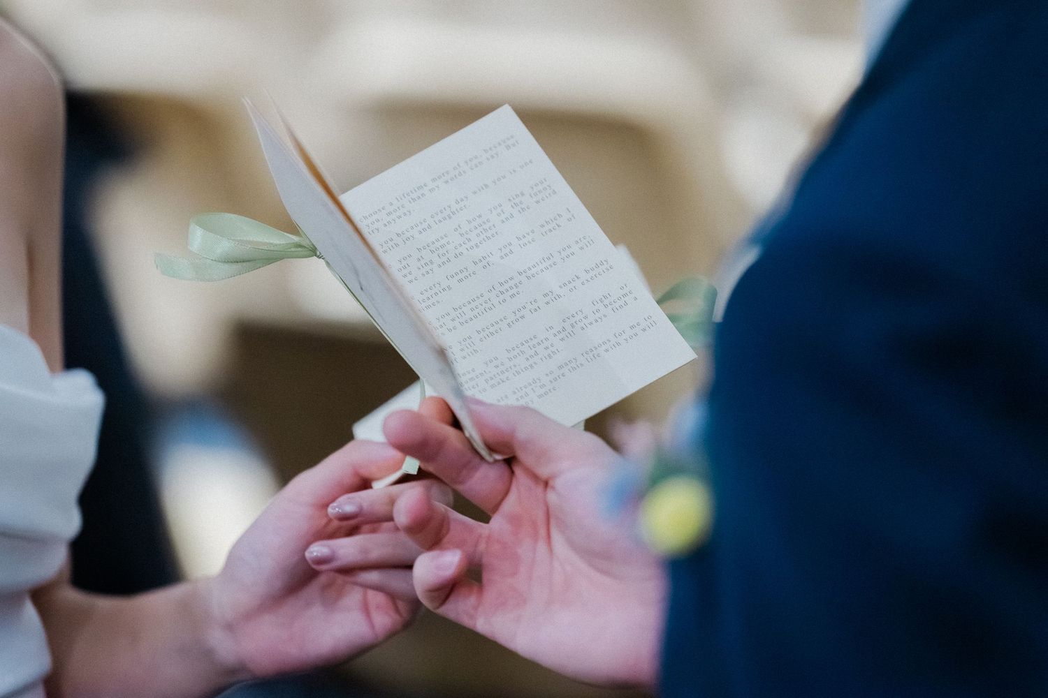 Couple exchanging wedding rings during ceremony while holding vows booklet together.
