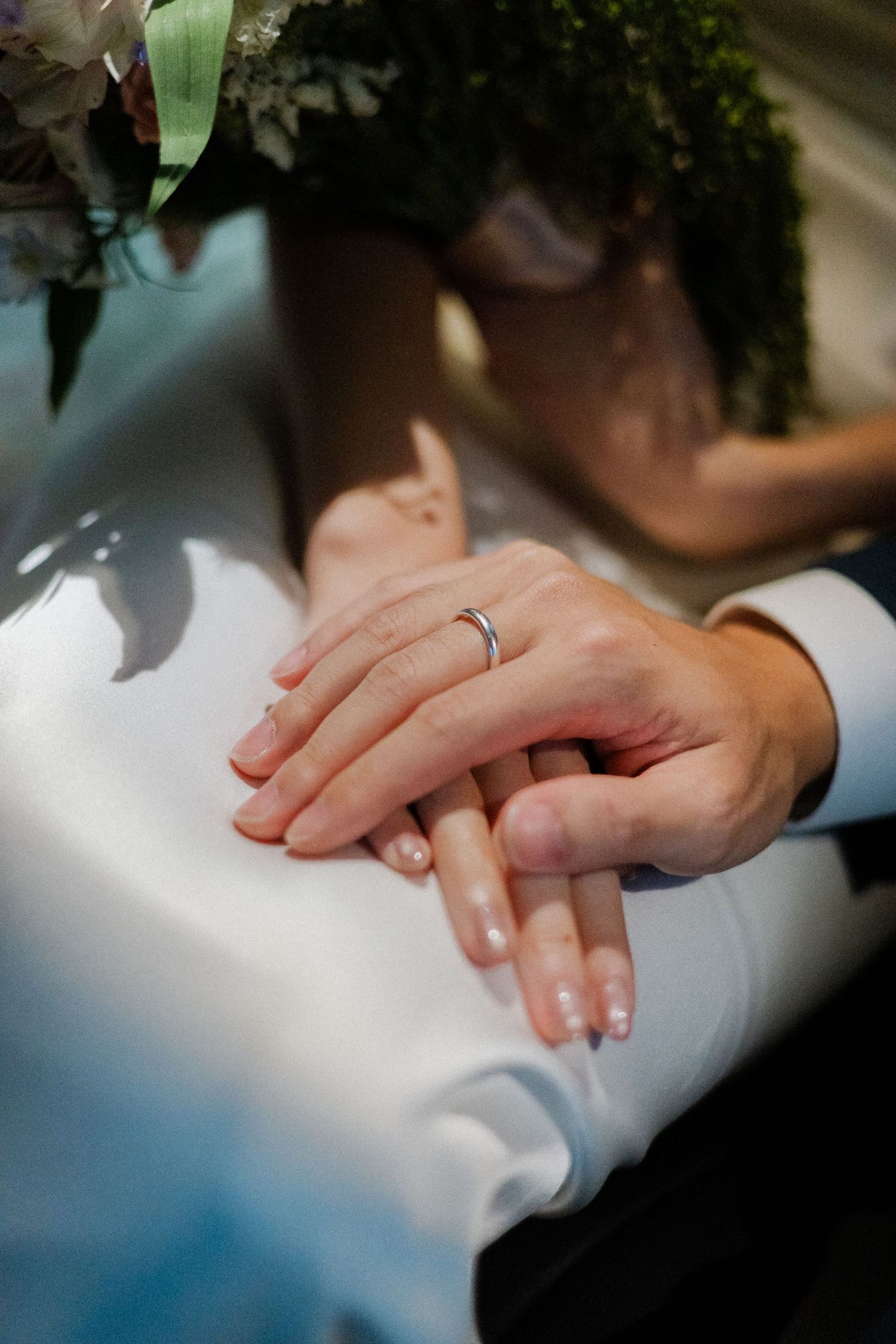 Bride and groom hands with wedding ring resting on white wedding dress.