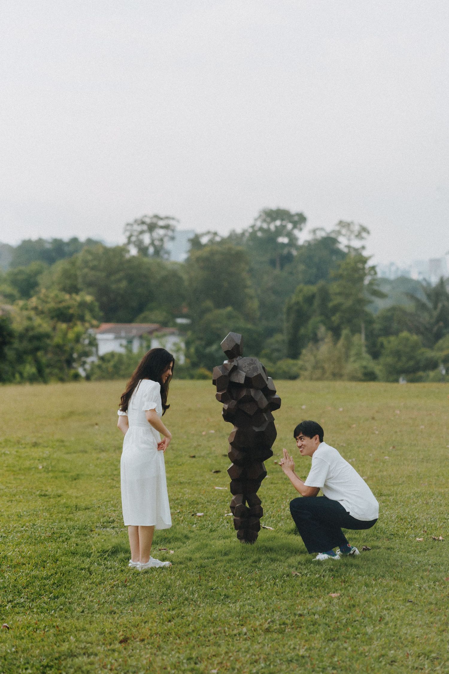 A couple poses for engagement photos with photographers in a grassy field.