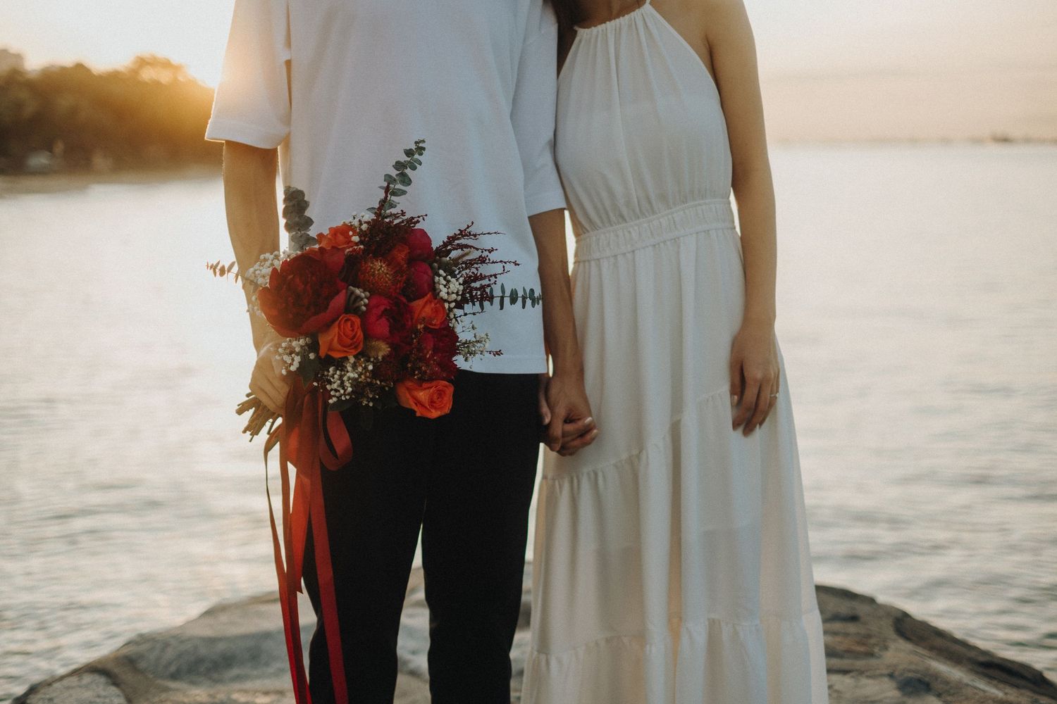 An intimate sunset beach wedding photoshoot featuring a couple near the water's edge in white and black attire.