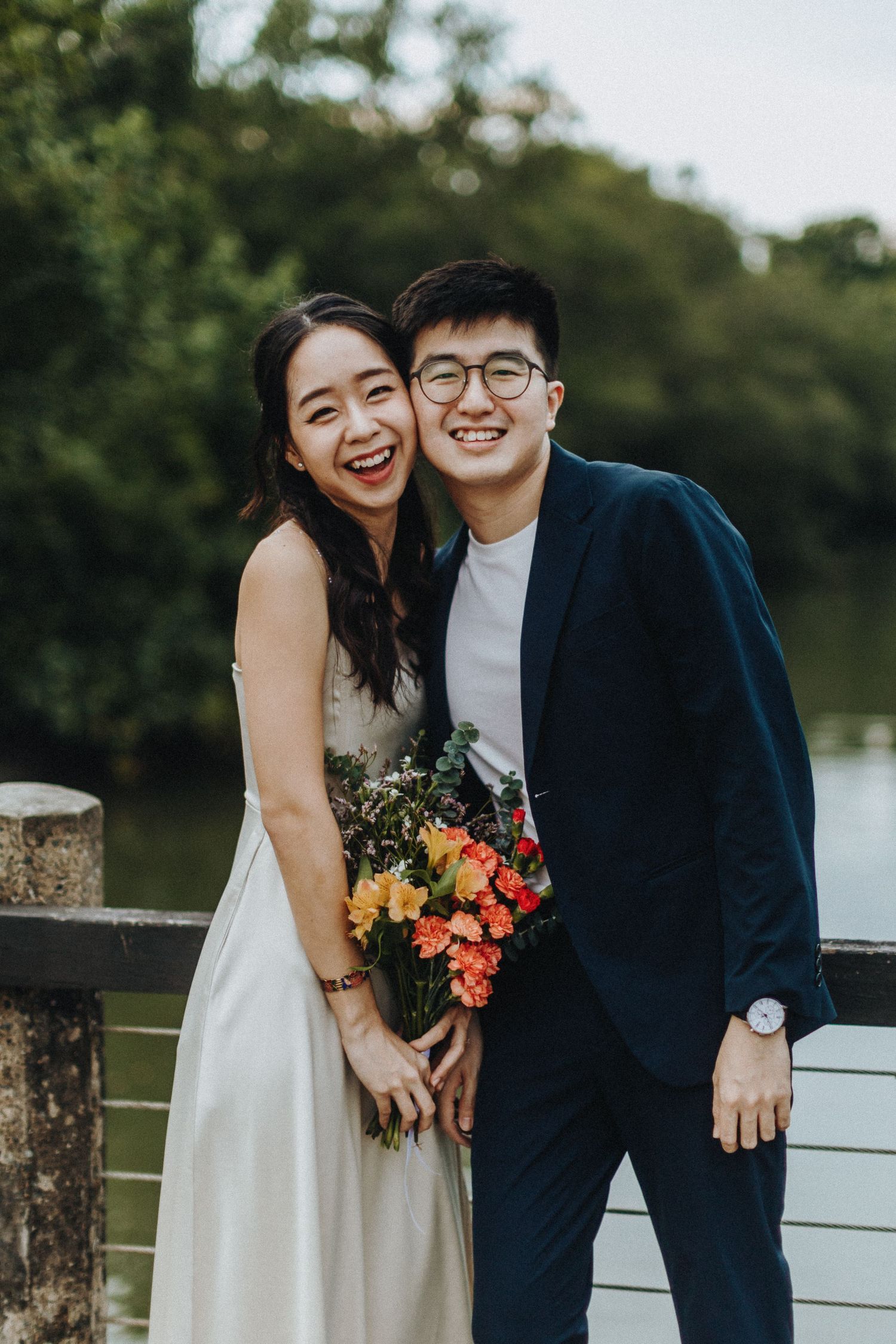 A couple shares a candid laugh while posing with colorful flowers during their waterfront engagement session.