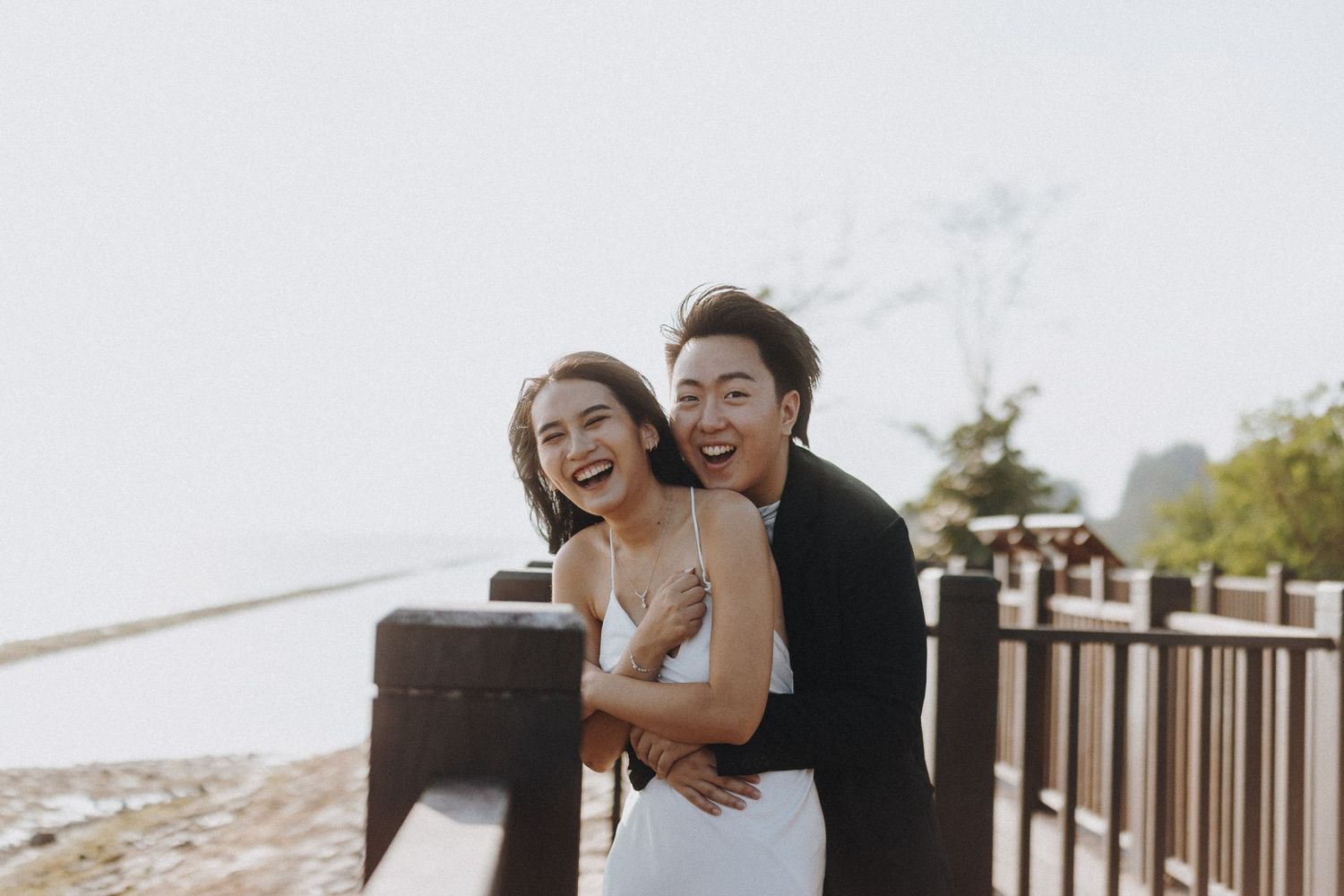 Couple sharing laughter while sitting on wooden deck overlooking the beach.