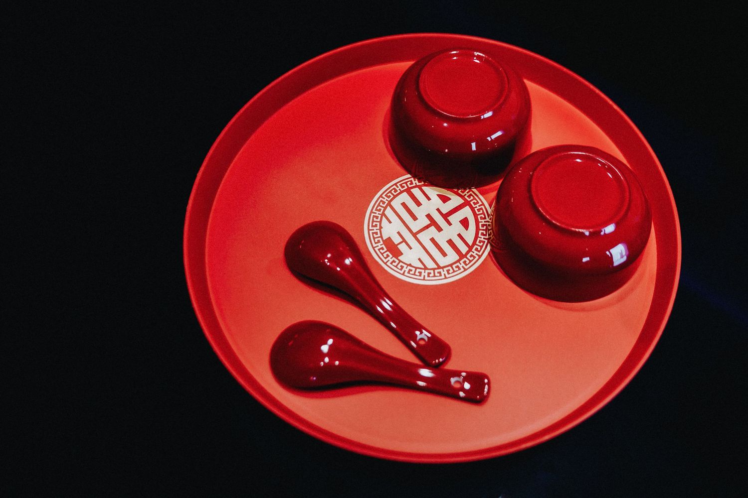 A red lacquerware serving tray with matching bowls and spoons arranged on a dark background.