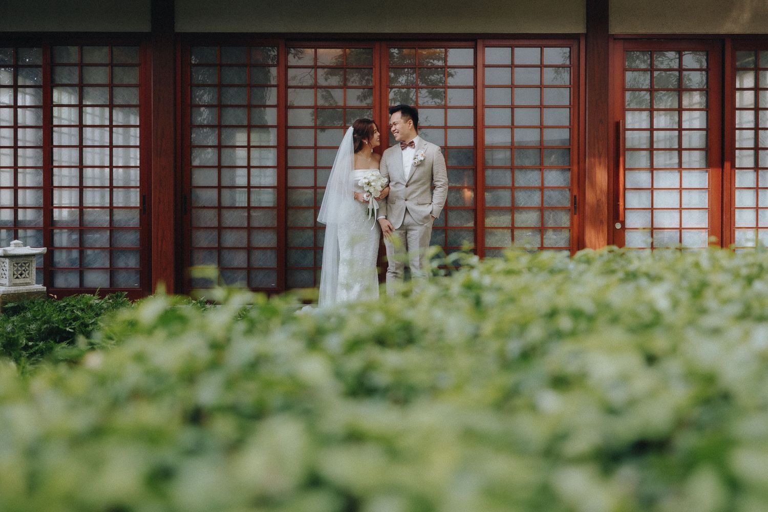 Wedding couple poses in front of Japanese garden with traditional architecture.