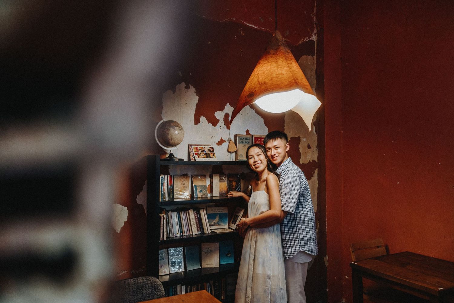 A couple poses together in a cozy library setting with warm lighting and bookshelves.
