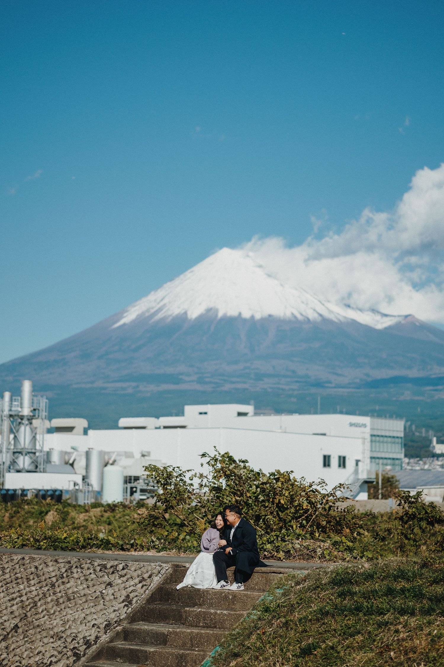 Couple sitting on stone steps with Mount Fuji and industrial buildings in the background in Japan.