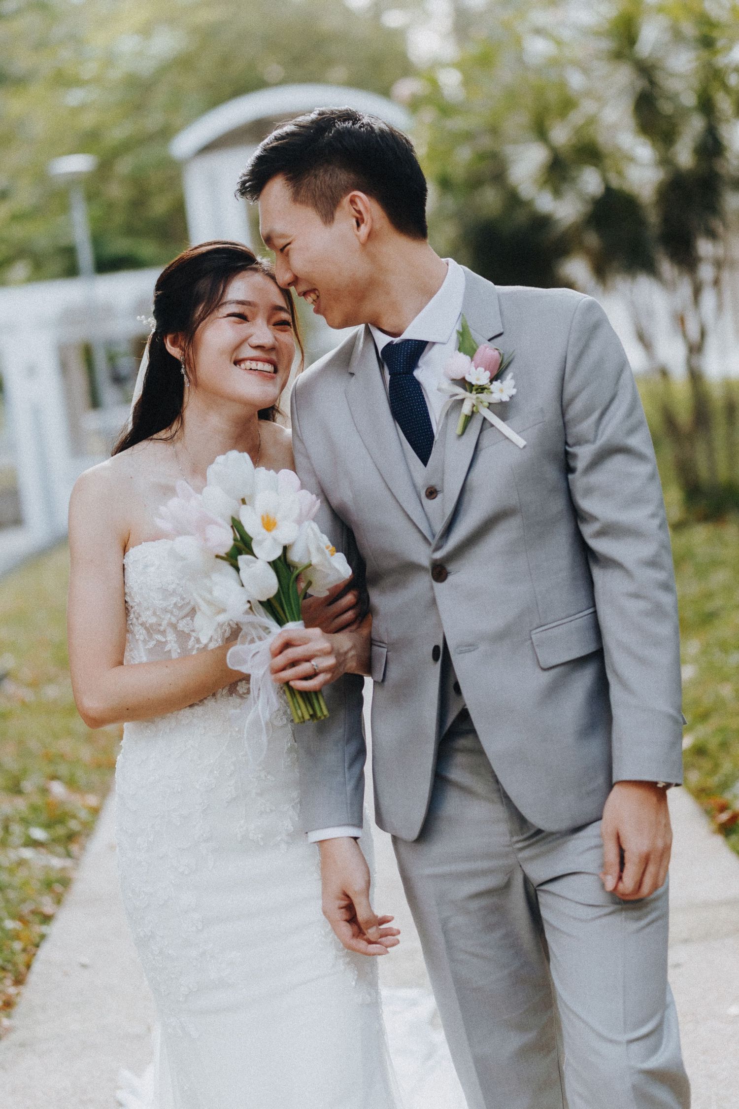 A couple shares intimate candid moments in their wedding attire against a garden backdrop.