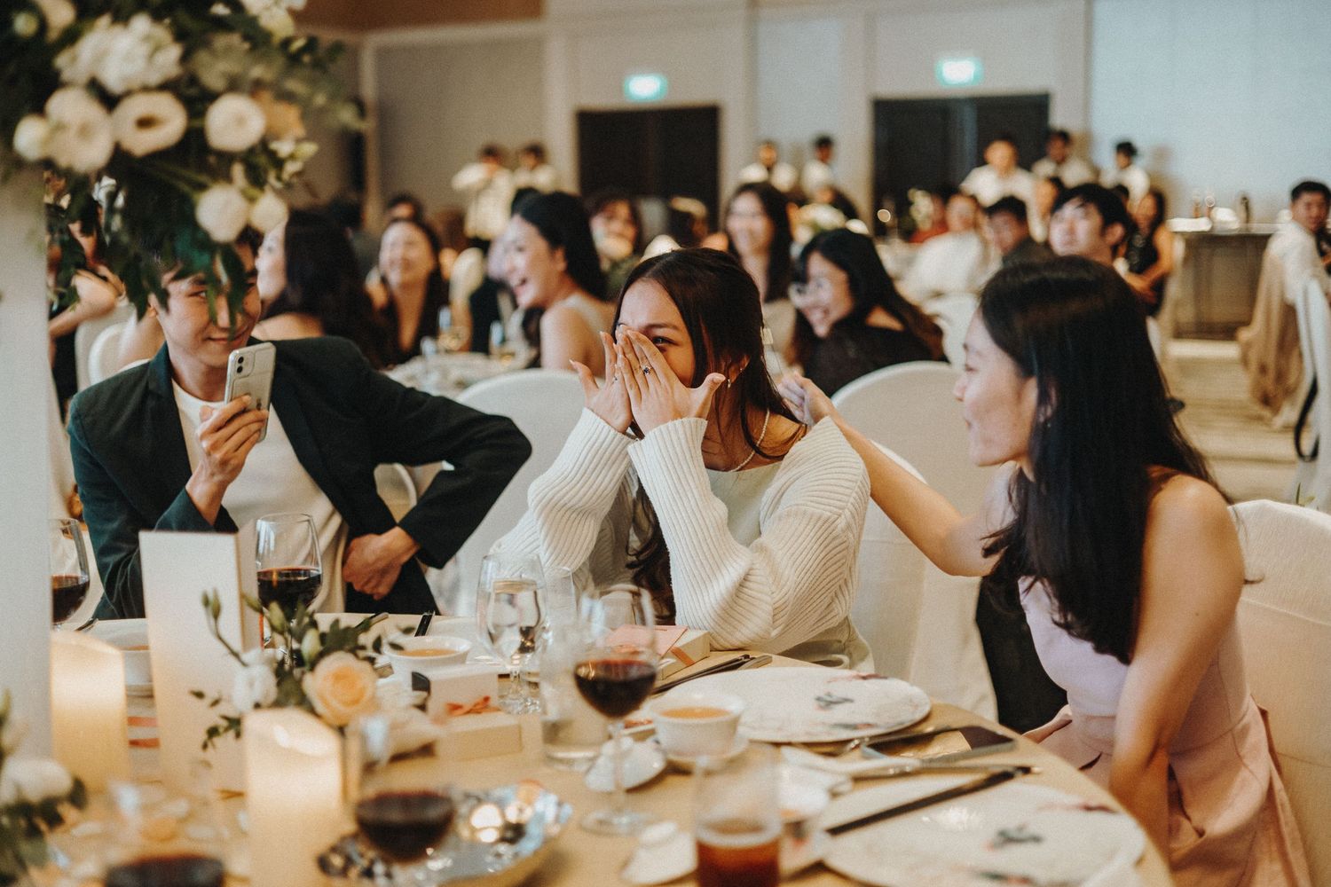 Wedding reception banquet hall with long tables decorated with white floral centerpieces and candlelight.