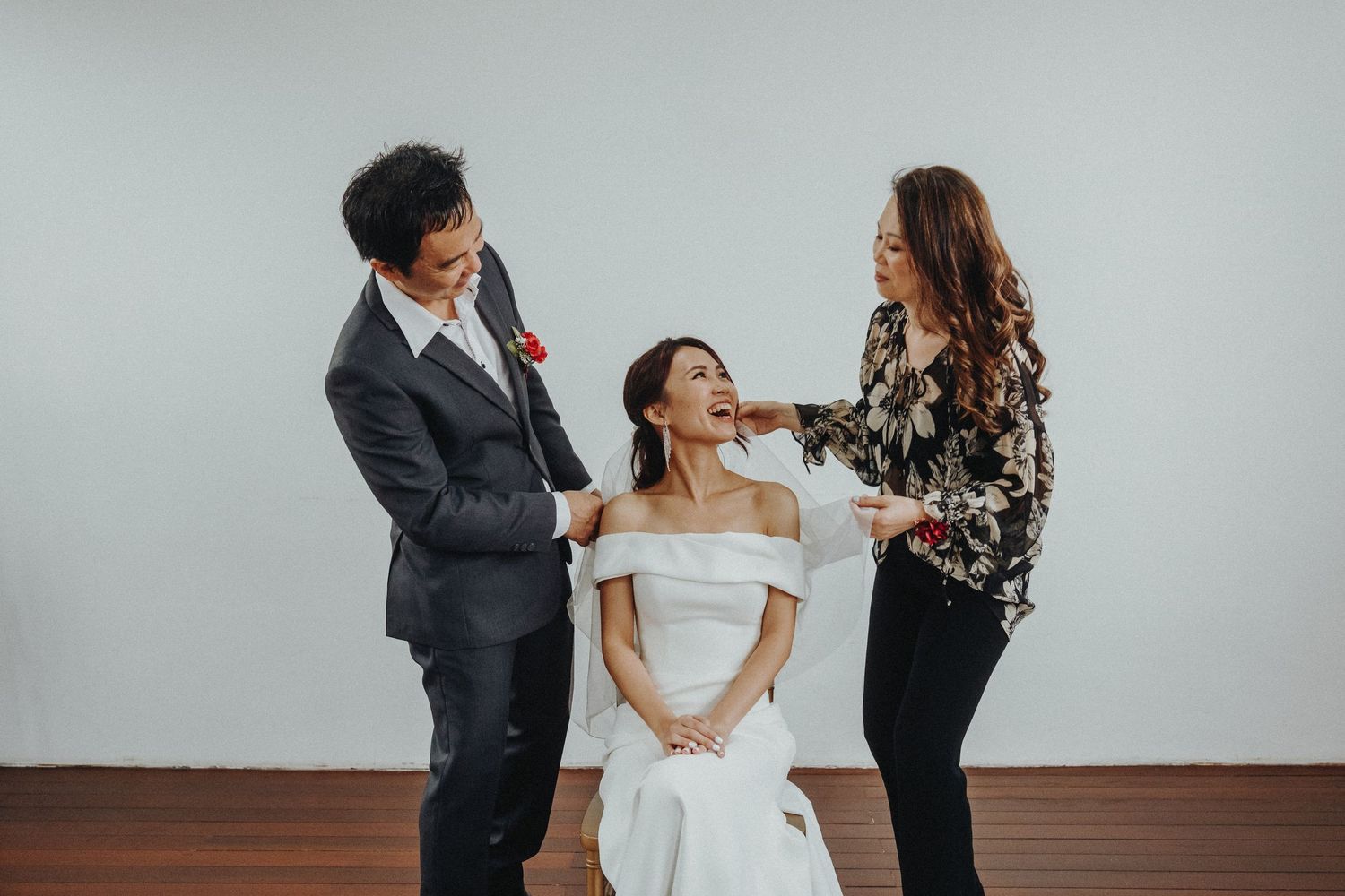 Behind the scenes bridal preparation moment with makeup artist and hairstylist getting bride ready in white dress.