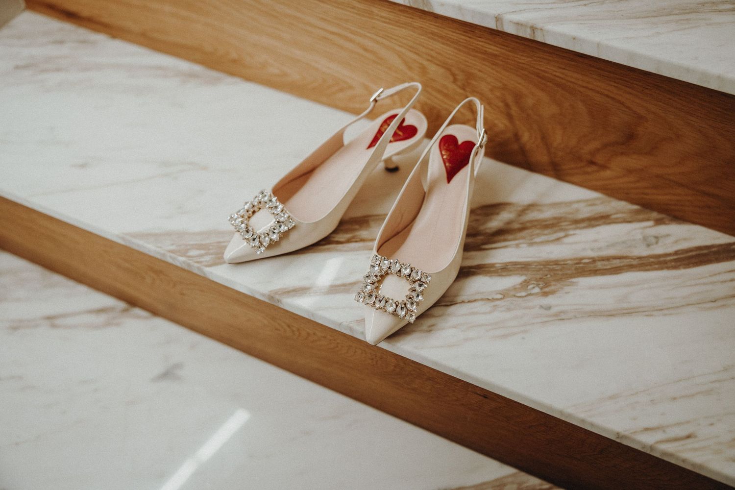 Elegant white bridal shoes with delicate pearl embellishments displayed on a light marble floor.