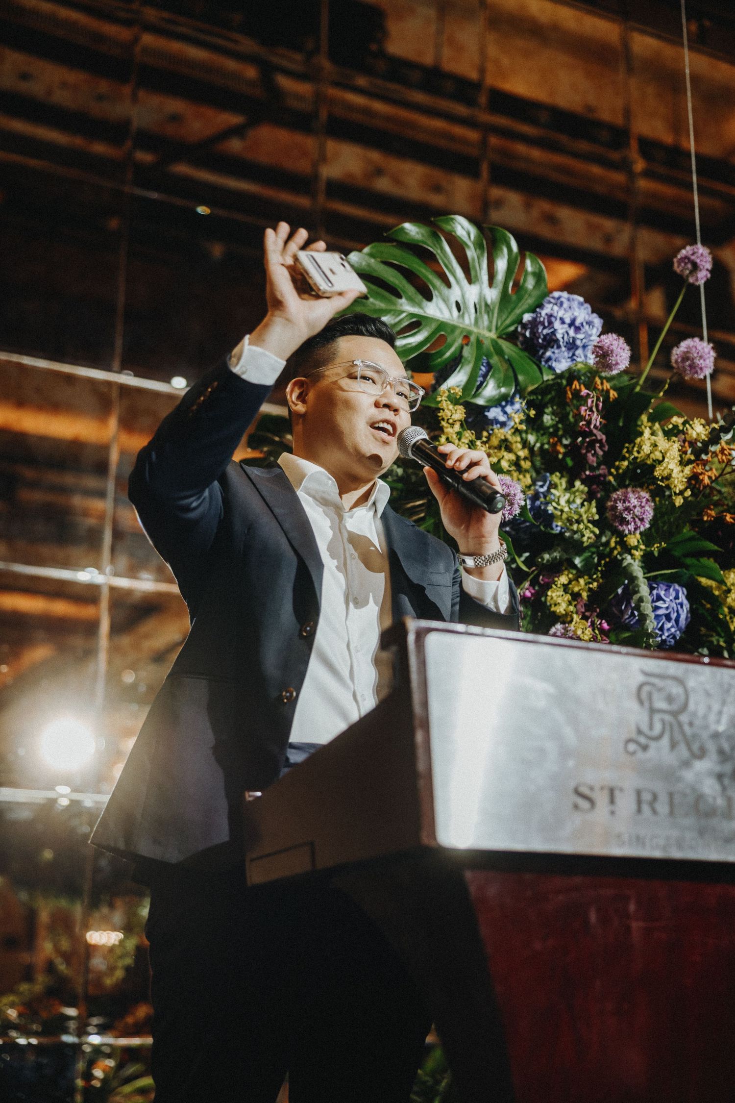 Person dancing under floral arrangements and decorative lighting at an indoor celebration venue.