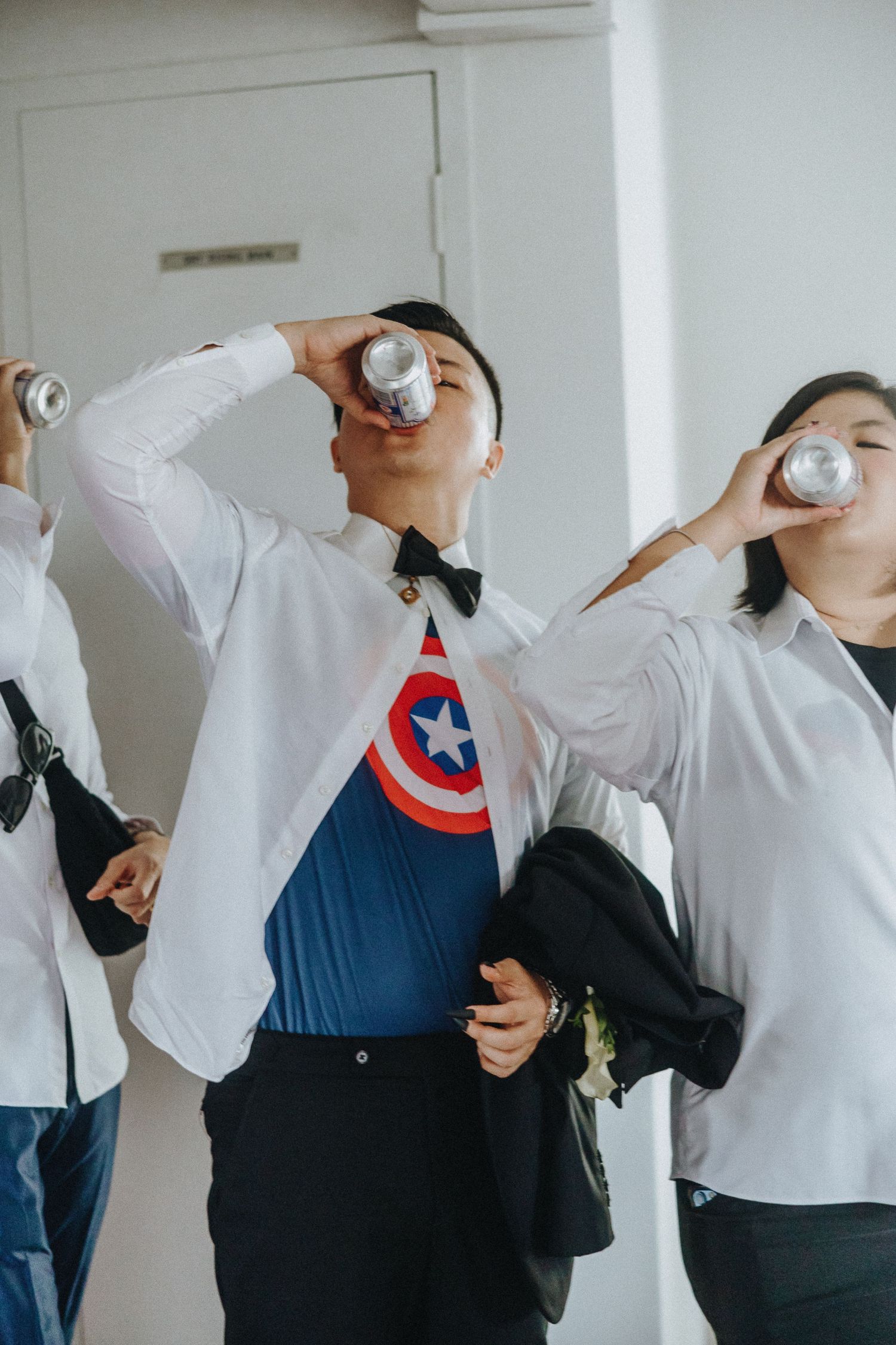 Group in white shirts and bow ties drinking from bottles, with one wearing a Captain America logo.