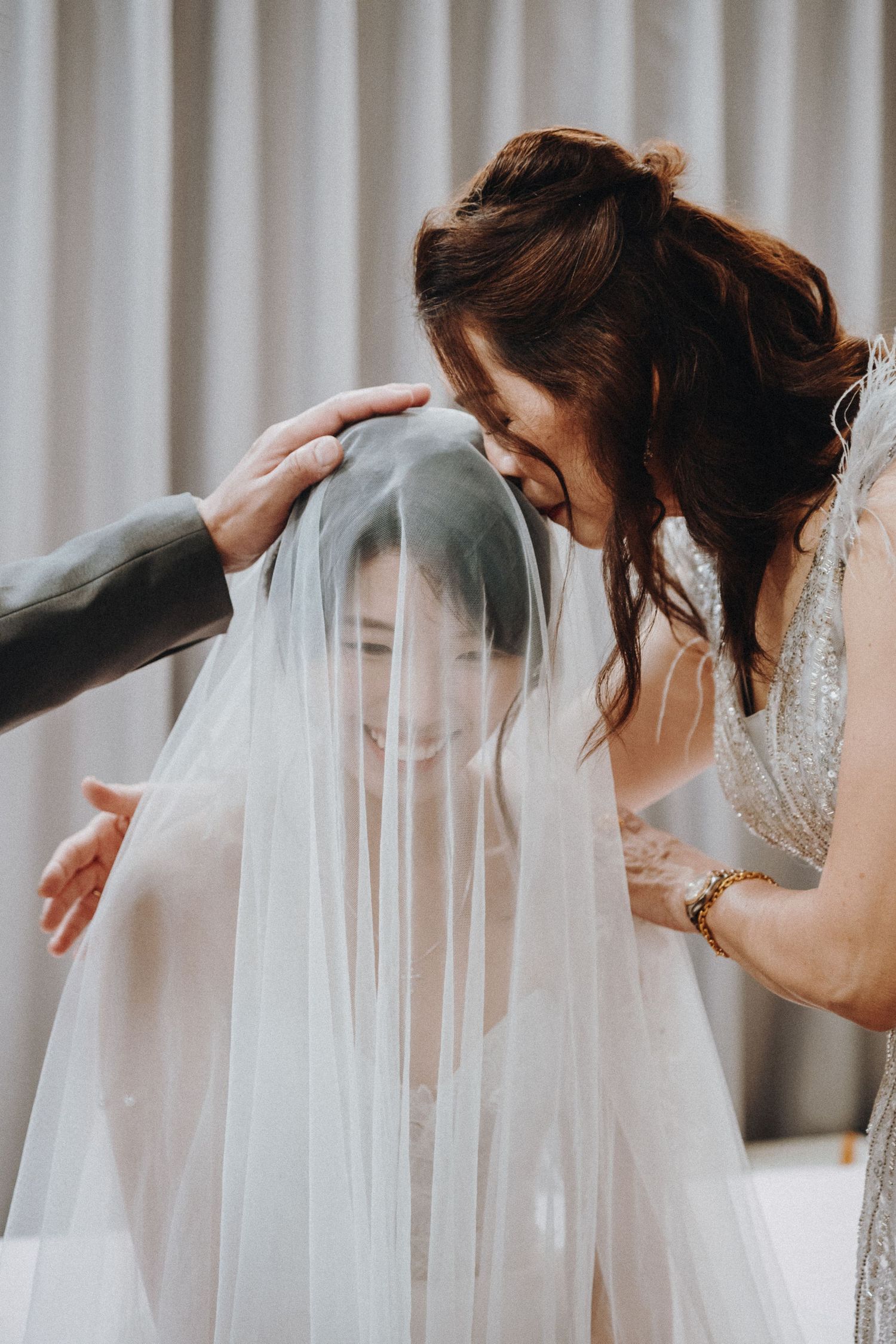 An intimate moment during wedding preparation as a veil is being adjusted in a softly lit room.