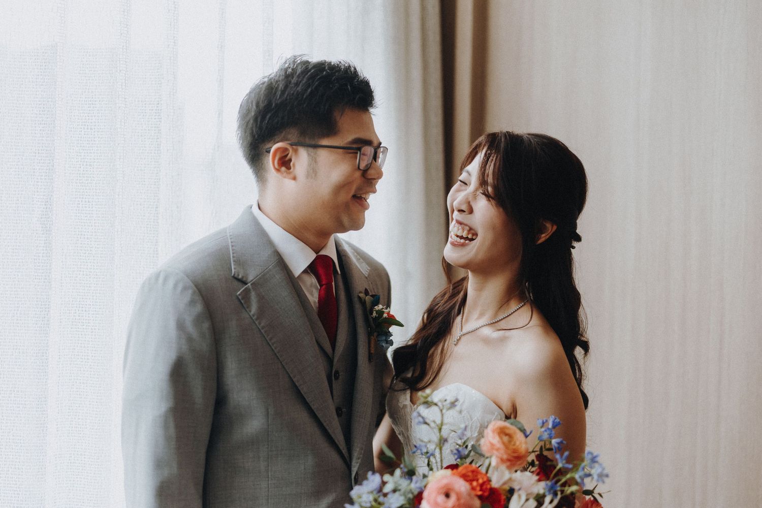 A happy couple in wedding attire share joyful moments together in a bright indoor setting.
