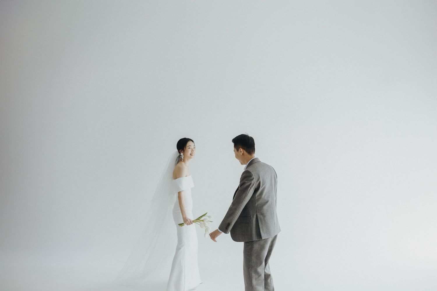 A minimalist wedding photo with a couple in elegant white and gray attire against a plain white background.