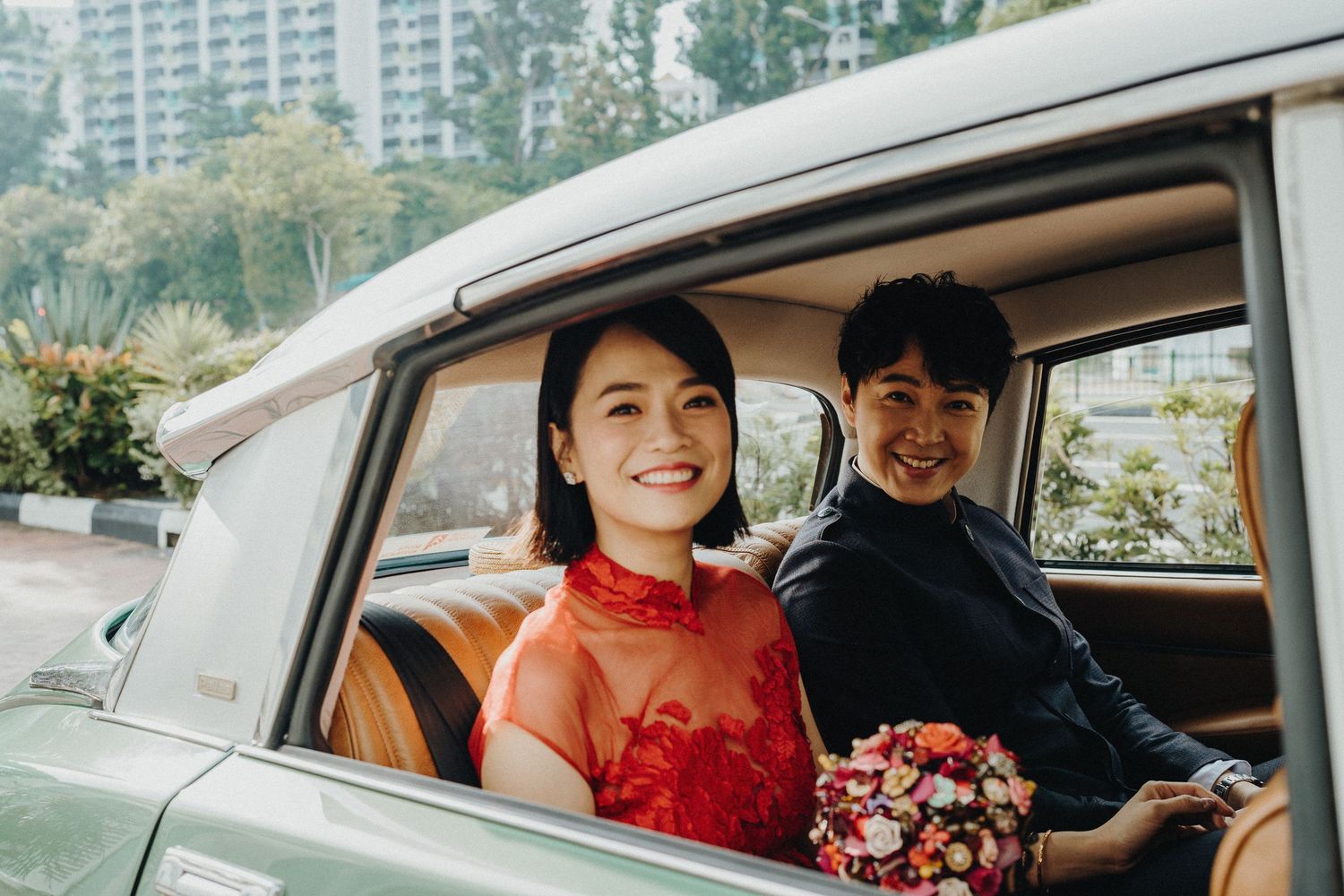 Happy couple seated in classic car with bride wearing red traditional dress.