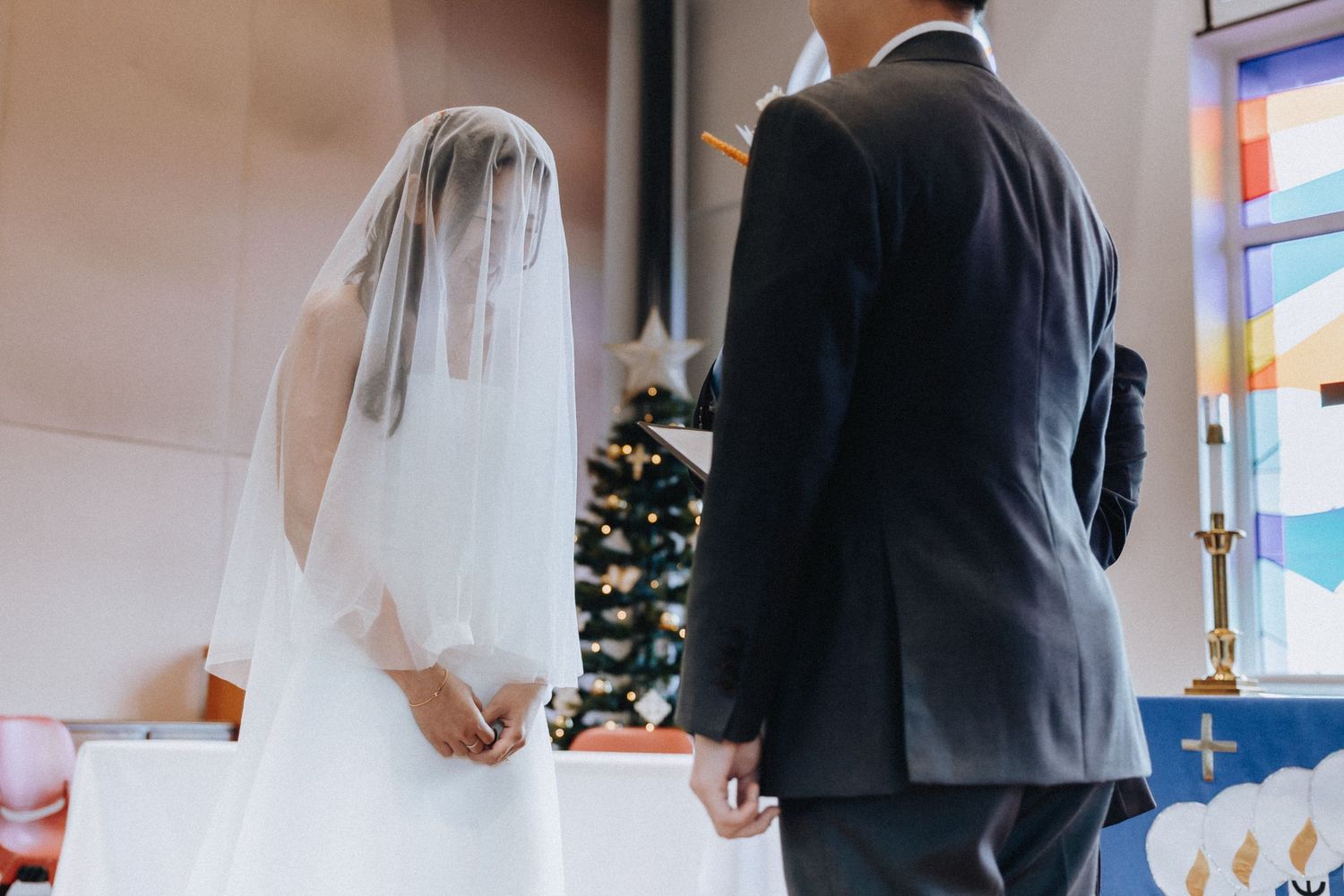 A bride in a white gown and veil stands beside her groom at the church altar during their ceremony.