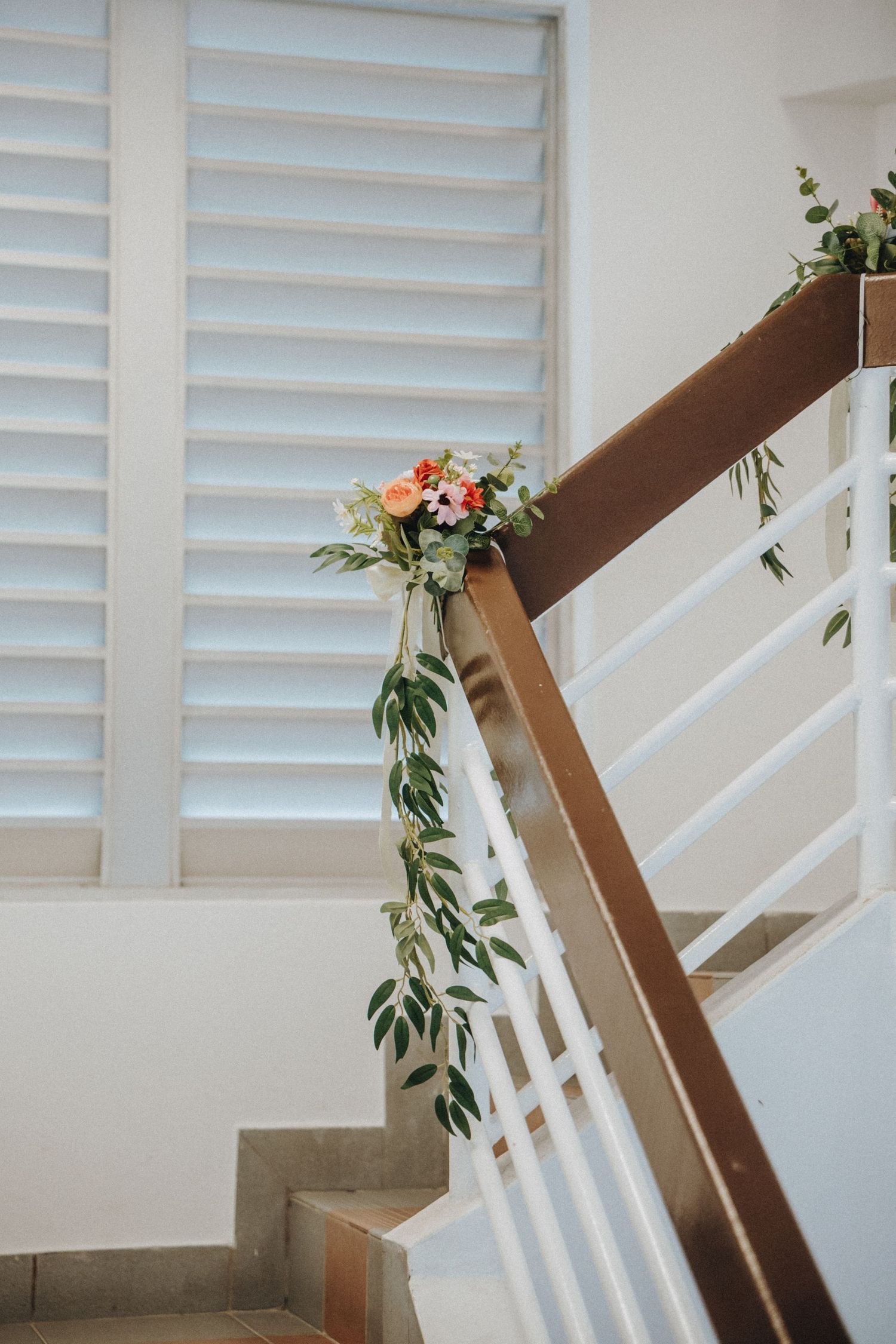 A floral garland with peach roses and greenery decorates a wooden staircase railing.