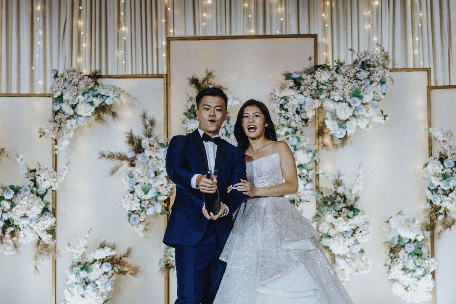 Wedding ceremony setup with elegant floral arch and white decor against a neutral backdrop.