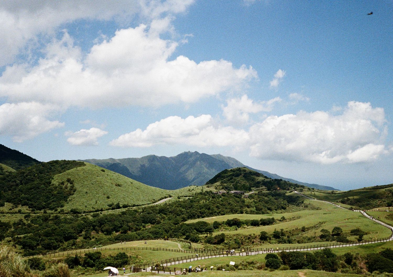 Rolling green hills and mountains under fluffy white clouds in a scenic pastoral landscape.