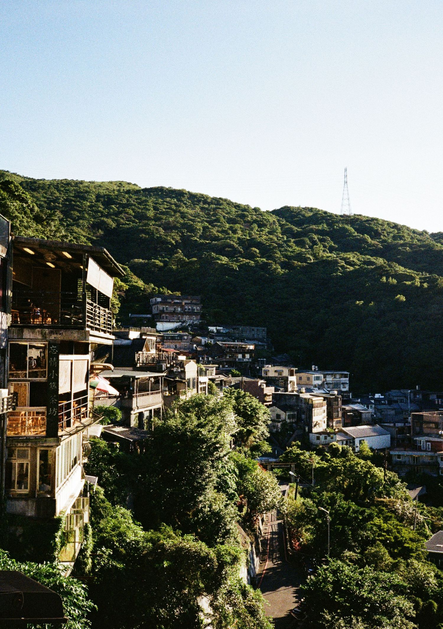 Scenic hillside view of traditional buildings nestled among lush green trees with mountains in background.