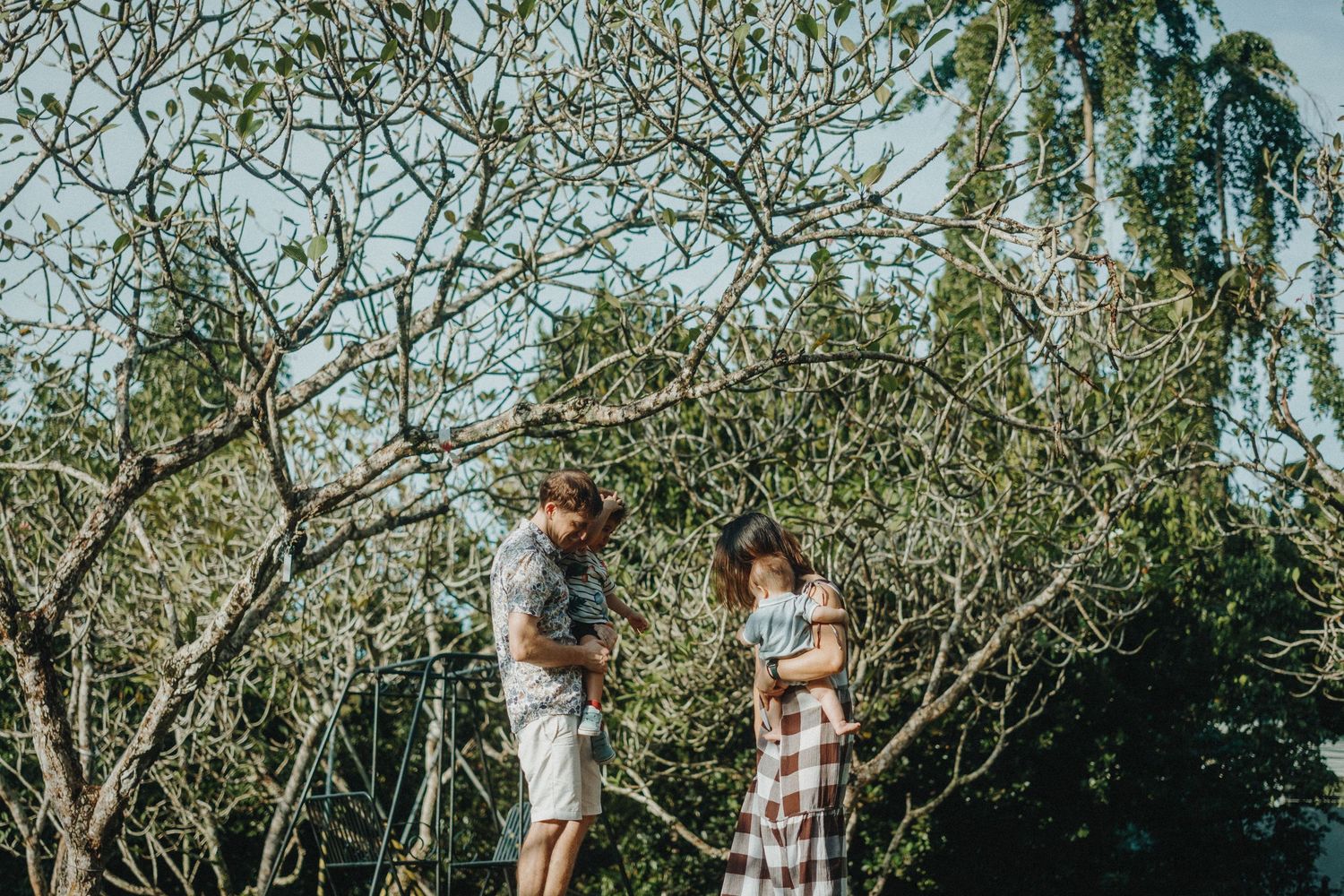 Family stands among bare tree branches in natural outdoor setting during daytime.