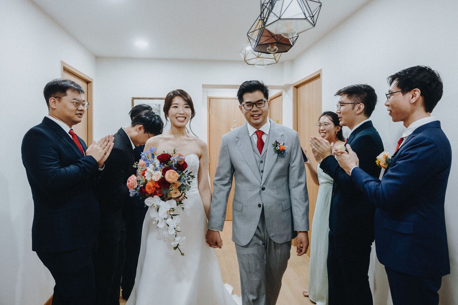 Wedding party members in grey suits celebrate and cheer during a traditional Chinese tea ceremony.