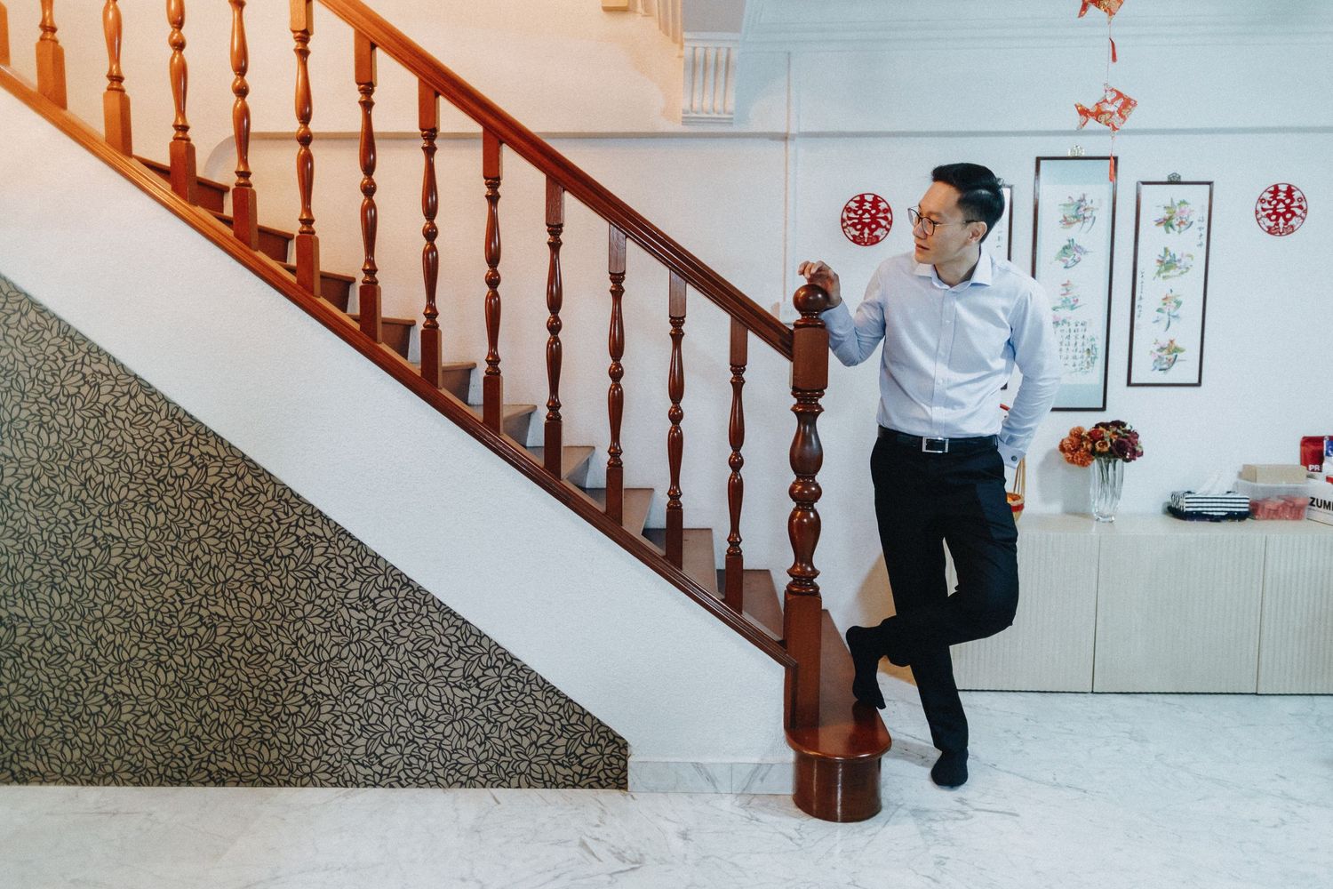 Someone in business attire leans casually against a wooden staircase railing in a modern interior setting.
