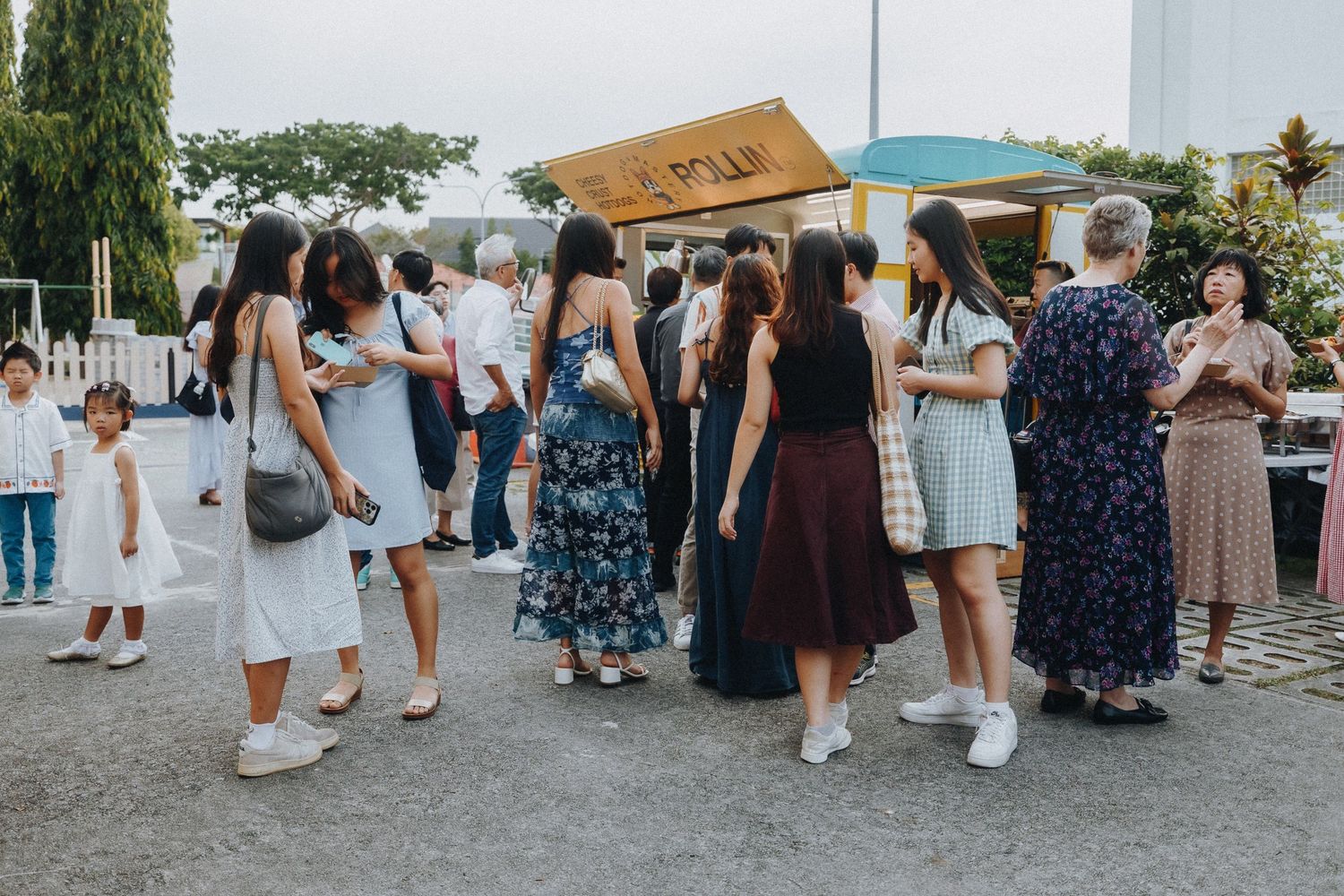 A group of people in casual attire gather outdoors near a food truck.