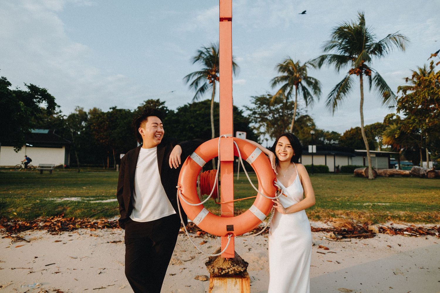 A couple poses with an orange life preserver on a tropical beach with palm trees.