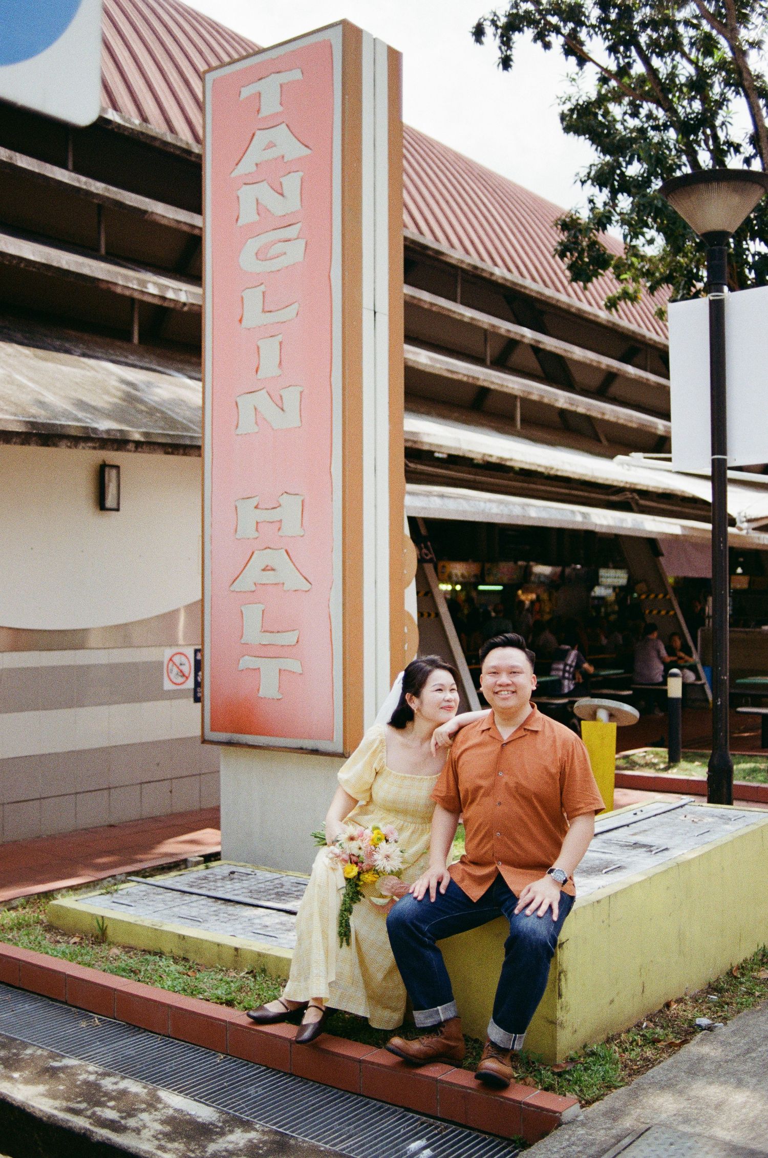 A couple poses together by a vintage-style Tanglin Halt sign in Singapore.