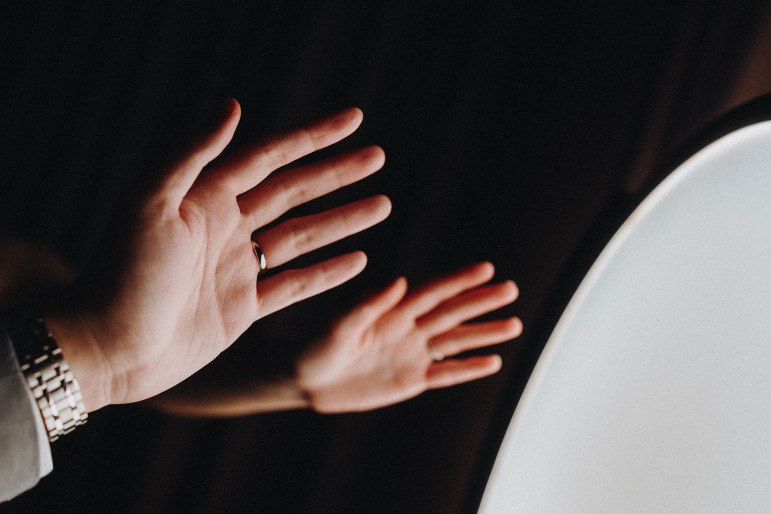 Close-up shot of hands reaching toward a white surface against a dark background.