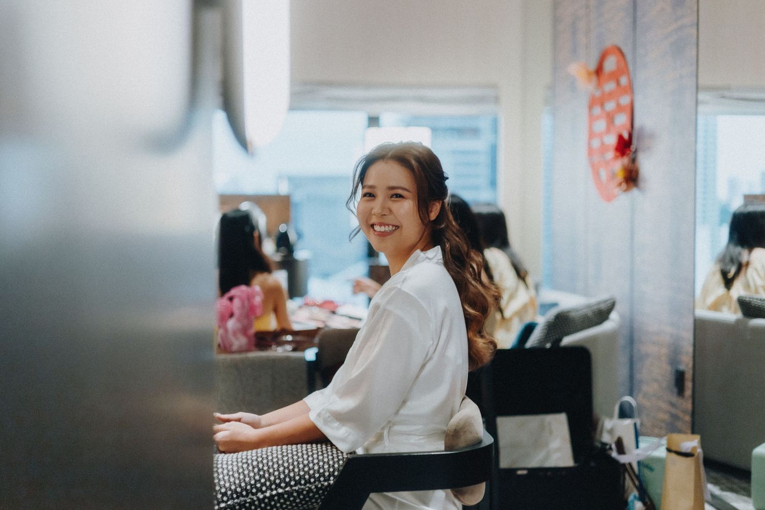 Someone in a white collared shirt smiles while working at a desk in a bright office space.