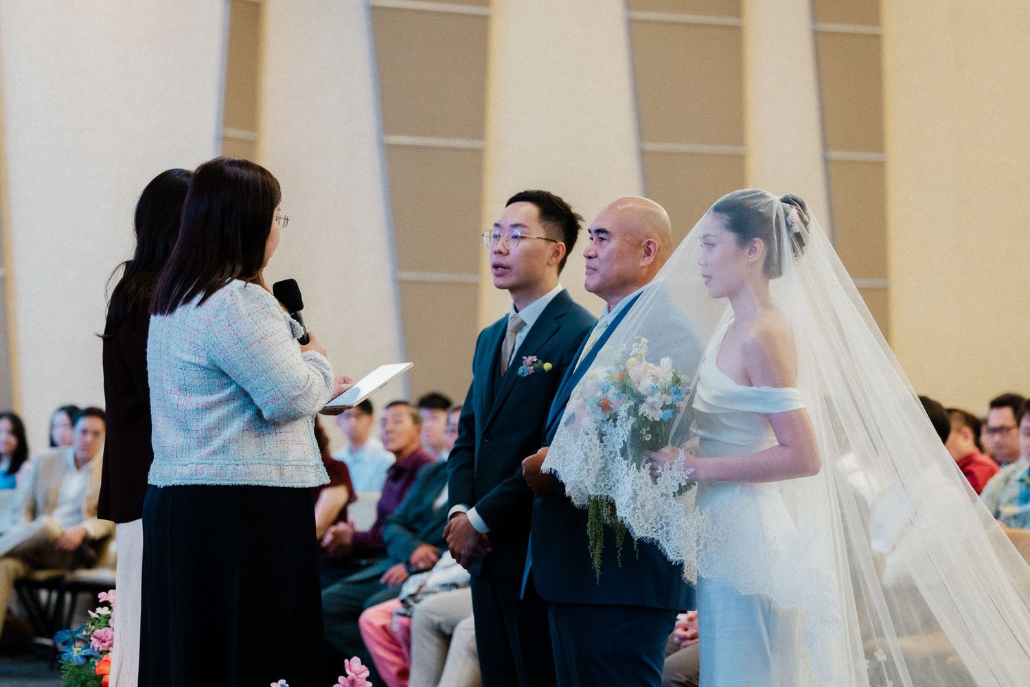 Wedding ceremony with bride in off-shoulder gown and veil standing at altar with groom and officiant.
