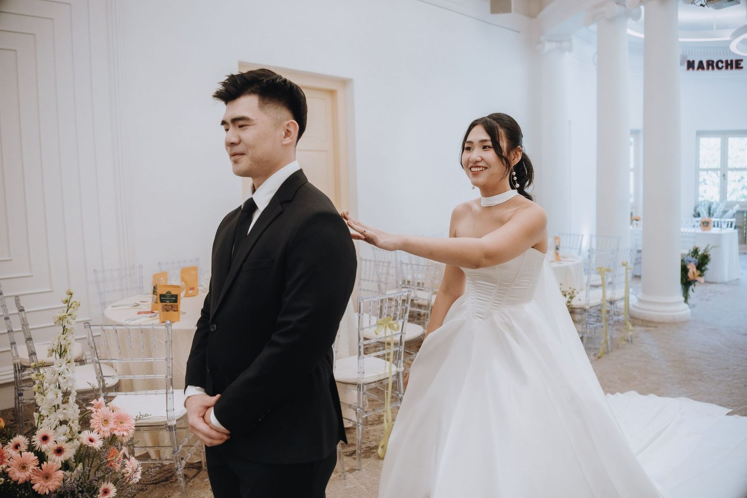 Smiling bride in white dress taps groom on shoulder during wedding first look moment.