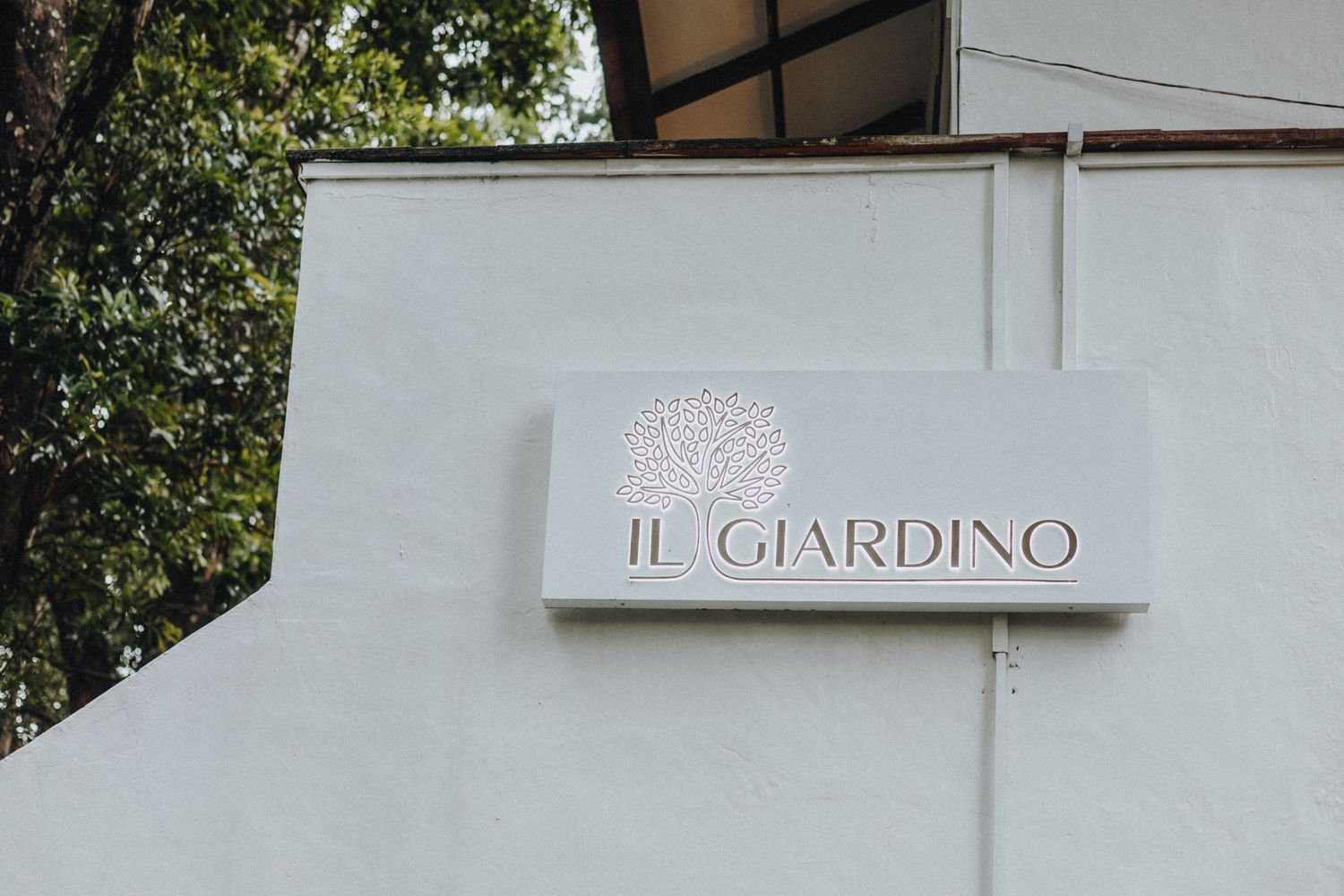 Il Giardino restaurant exterior sign mounted on white wall with tree logo.