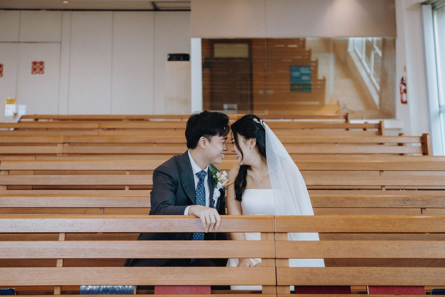 Romantic bride and groom share an intimate moment seated together in church pews.
