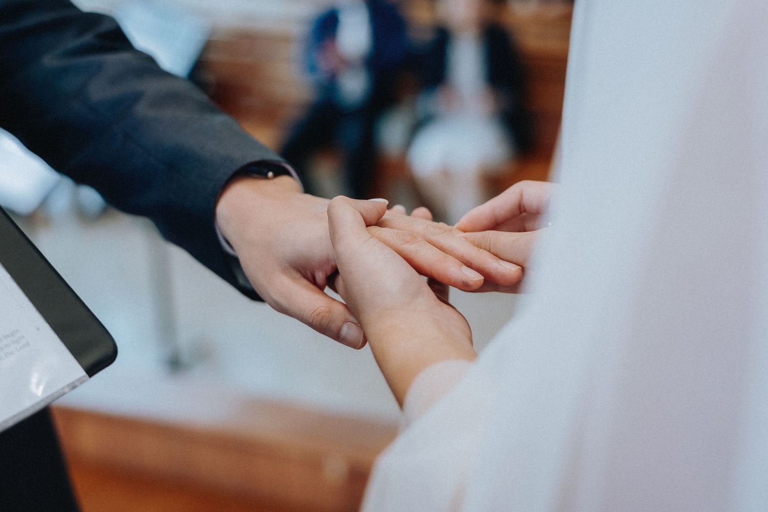 Groom places wedding ring on brides finger during intimate church ring exchange ceremony.