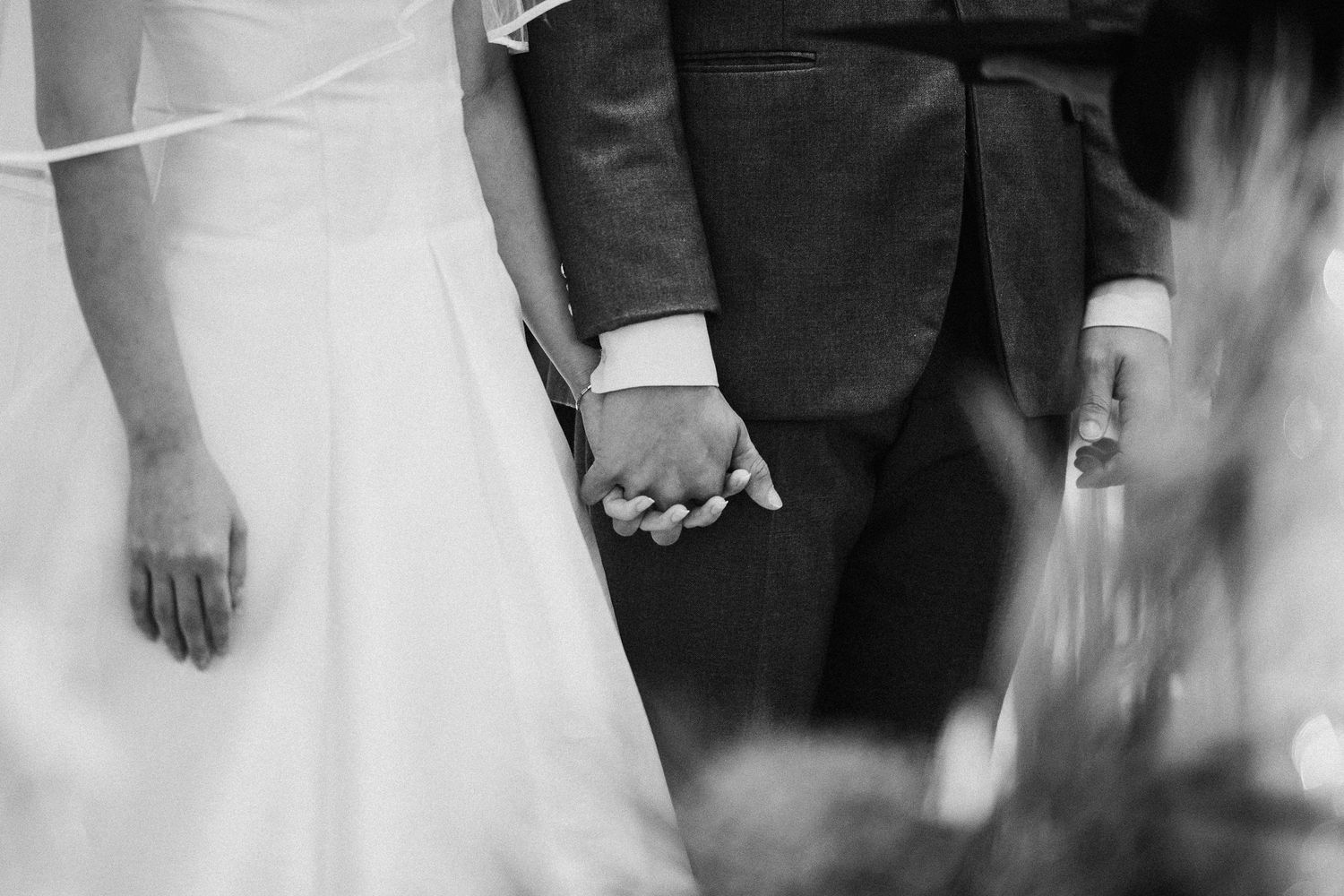 Black and white photo showing formal attire and hands clasped together during a wedding ceremony.