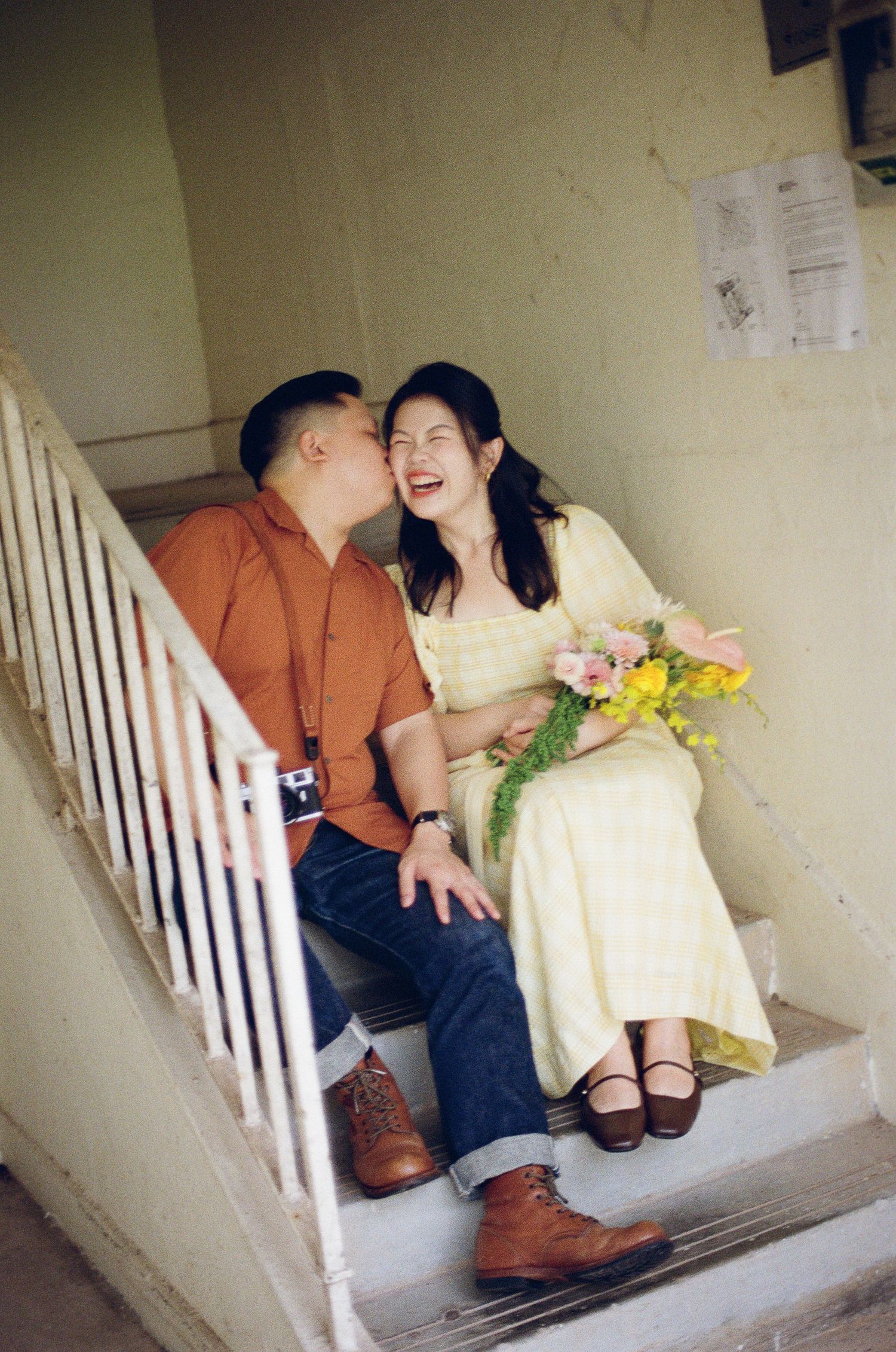 A candid moment of laughter shared on white stairs with a bouquet of flowers.