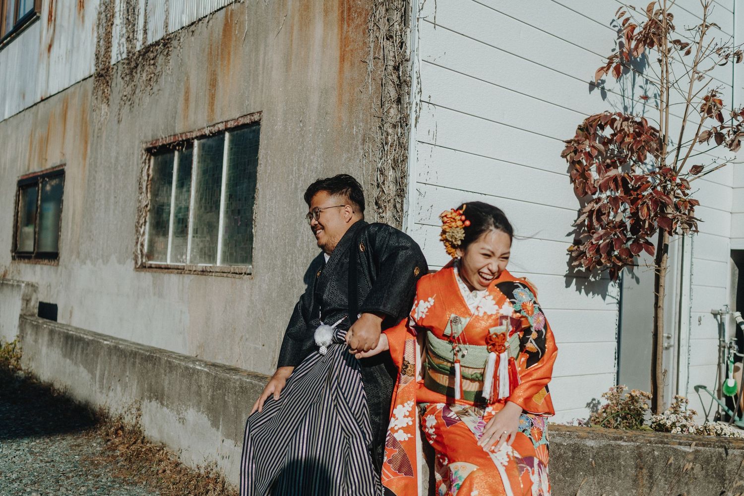 A couple in traditional Japanese attire walks together along an aged building exterior.