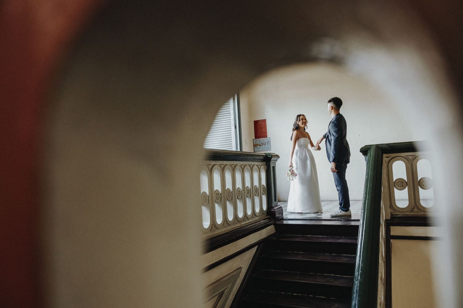 Wedding couple stands on vintage staircase with architectural details in dramatic lighting.