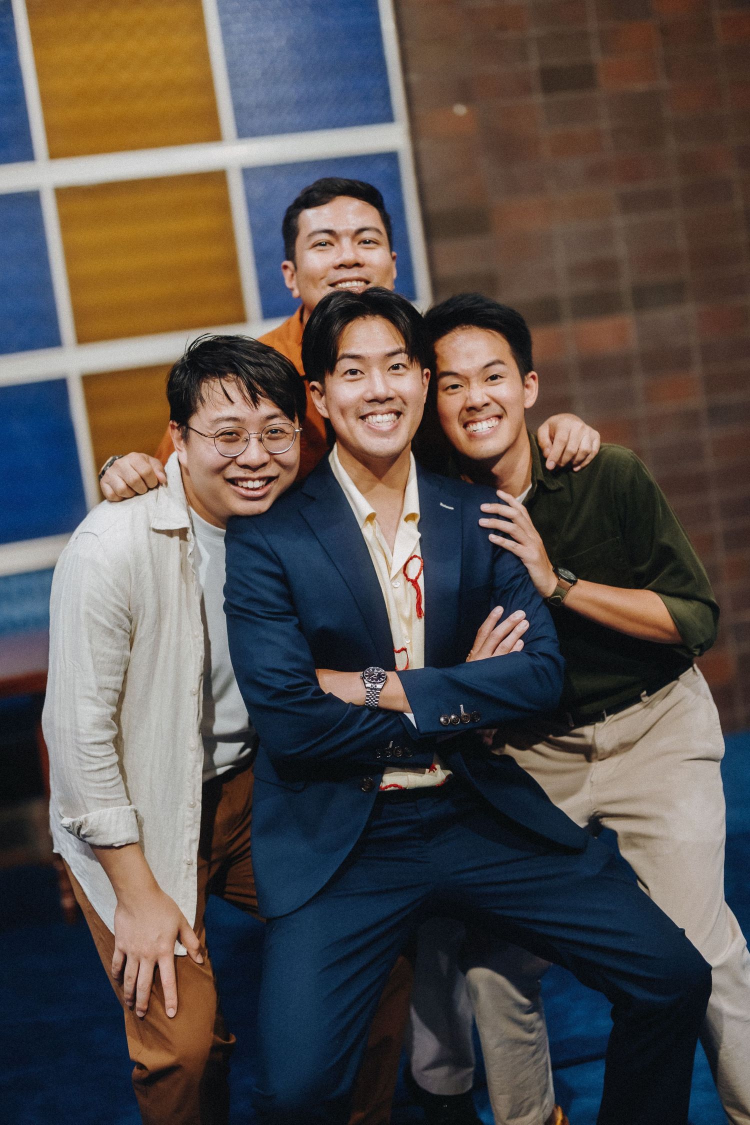 Three friends pose together in front of a colorful geometric wall display.