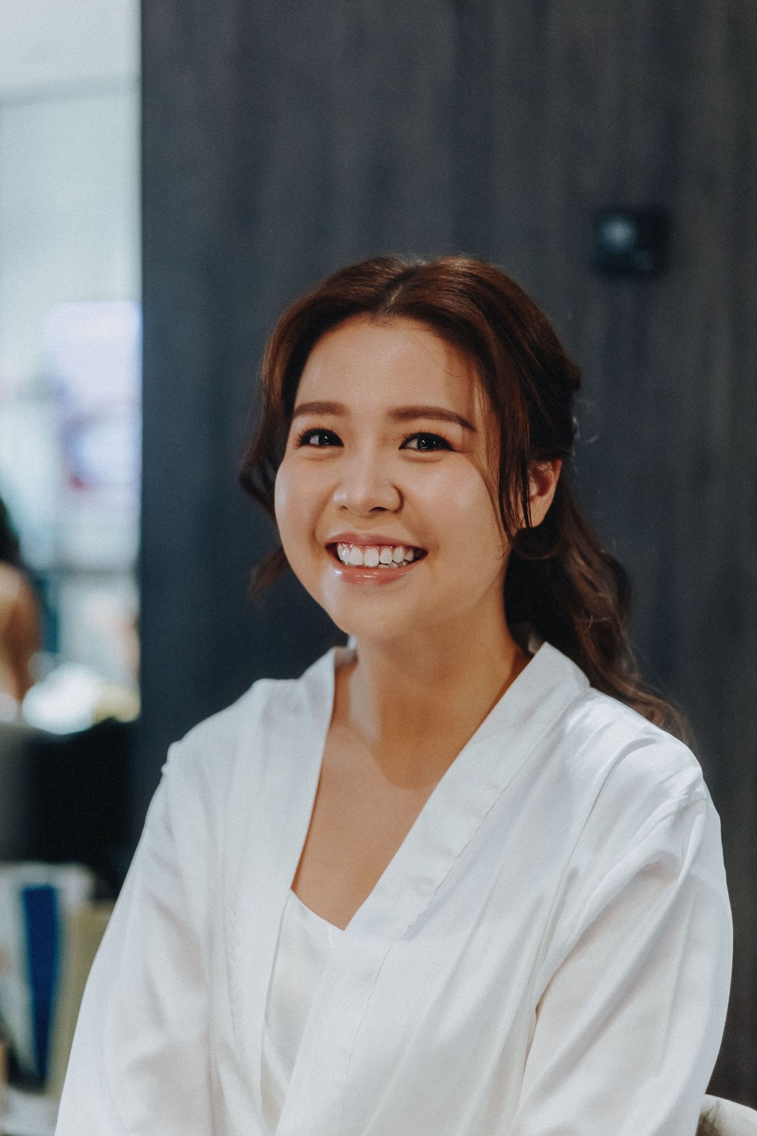 A person in a white robe smiles warmly while getting ready for a wedding ceremony.