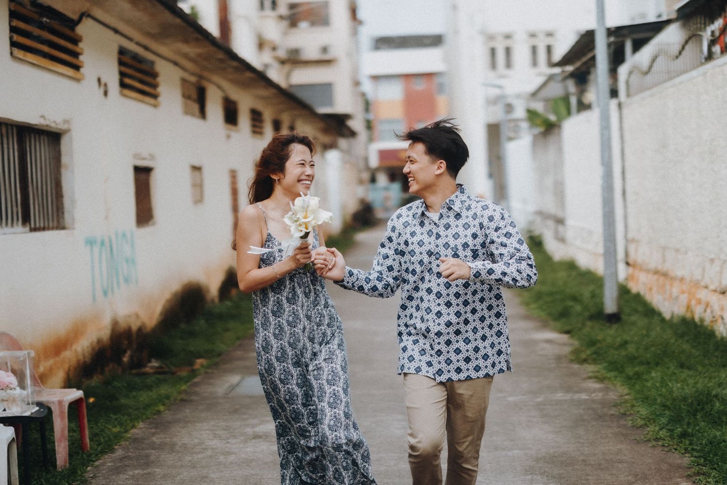 Couple walking down an urban alleyway lined with white buildings and grass.
